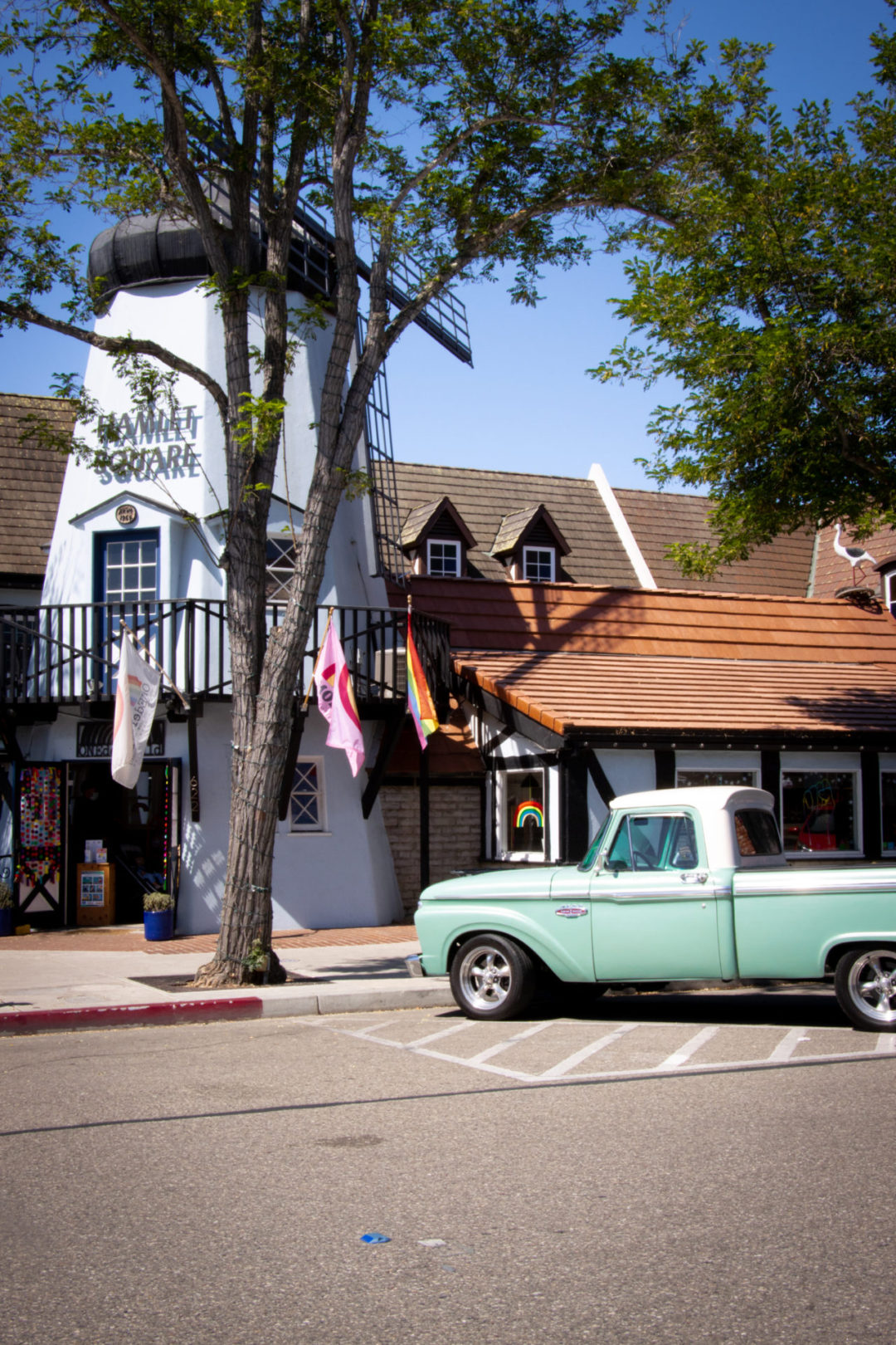 A building with an entrance fashioned like a white windmill with the sign "Hamlet Square" on top of it in Solvang, California
