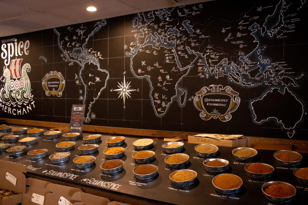Bowls of loose spices underneath a chalkboard map of the world at The Spice Merchant in Solvang, California