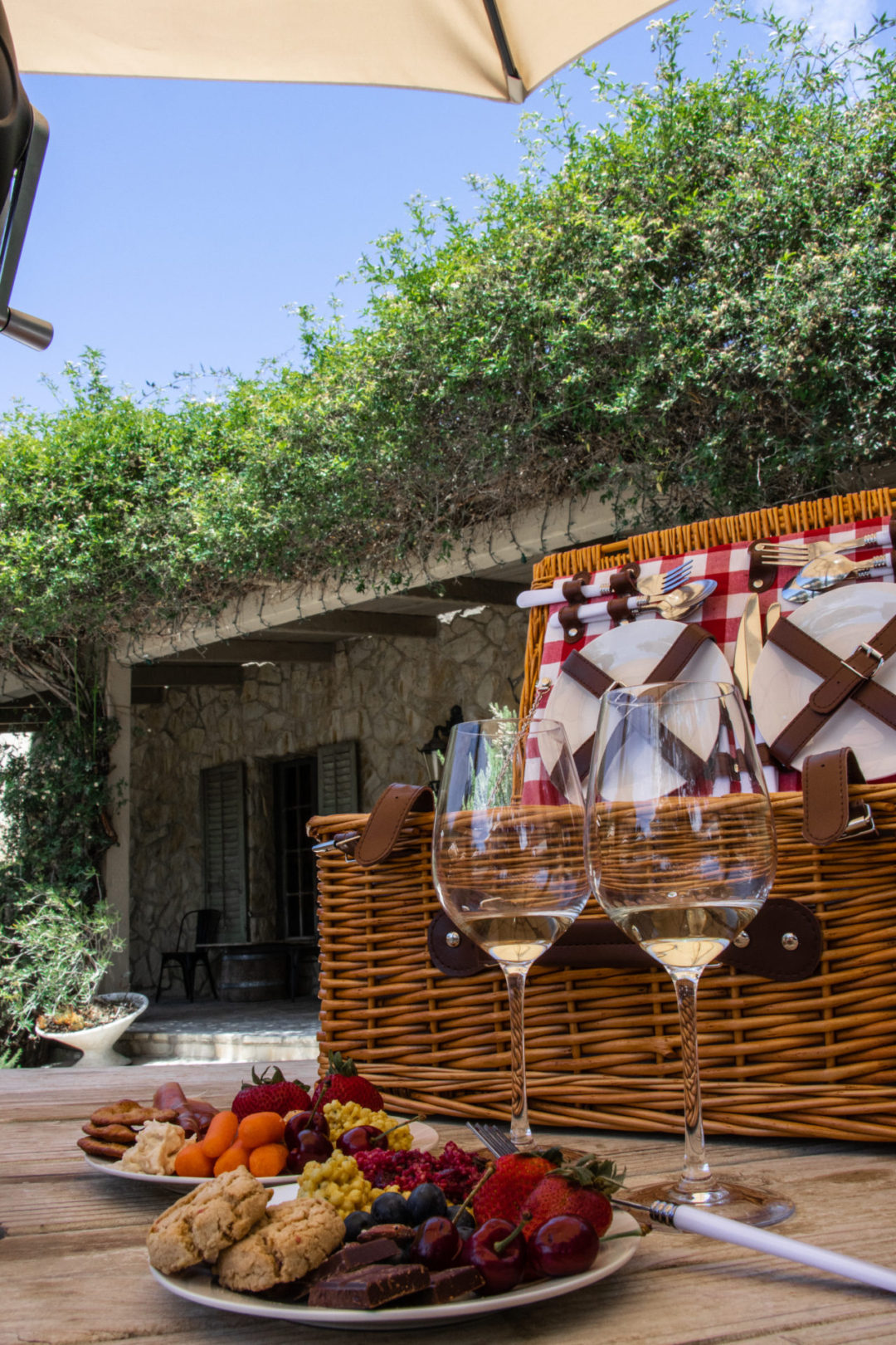 Two plates full of food and two glasses of white wine in front of a picnic basket at Sunstone Vineyards in Solvang, California