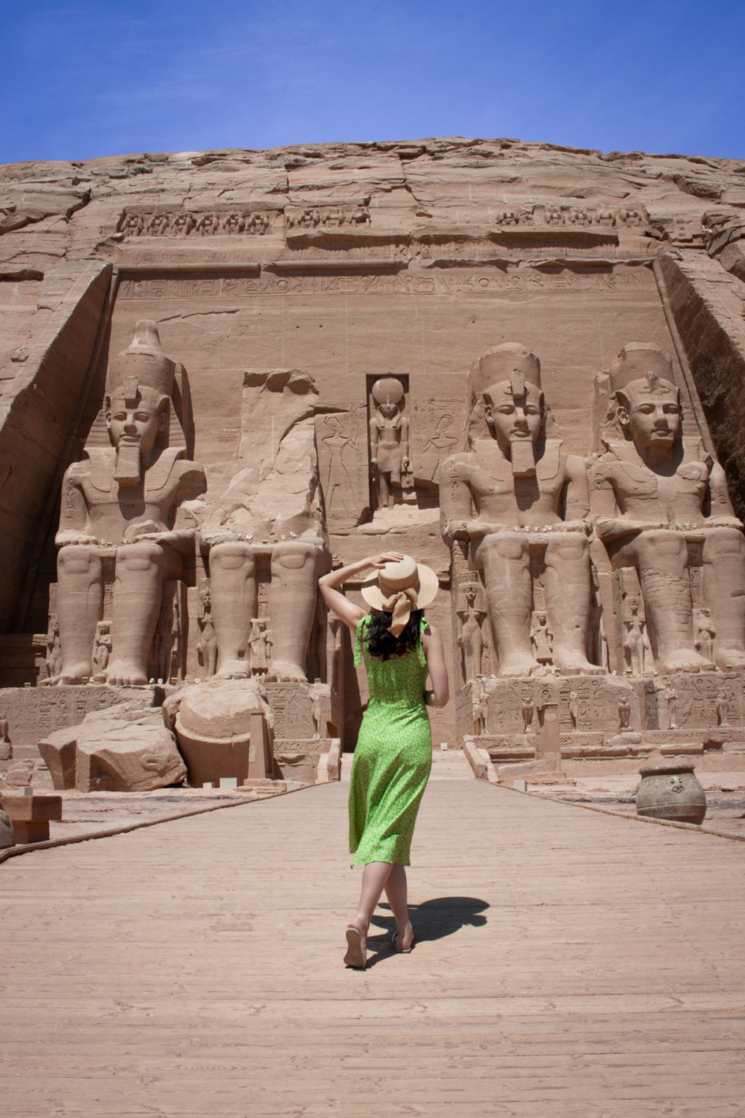 Travel Blogger Jordan Gassner holding onto a sunhat with her left hand while walking along the path to the Great Temple of Abu Simbel 