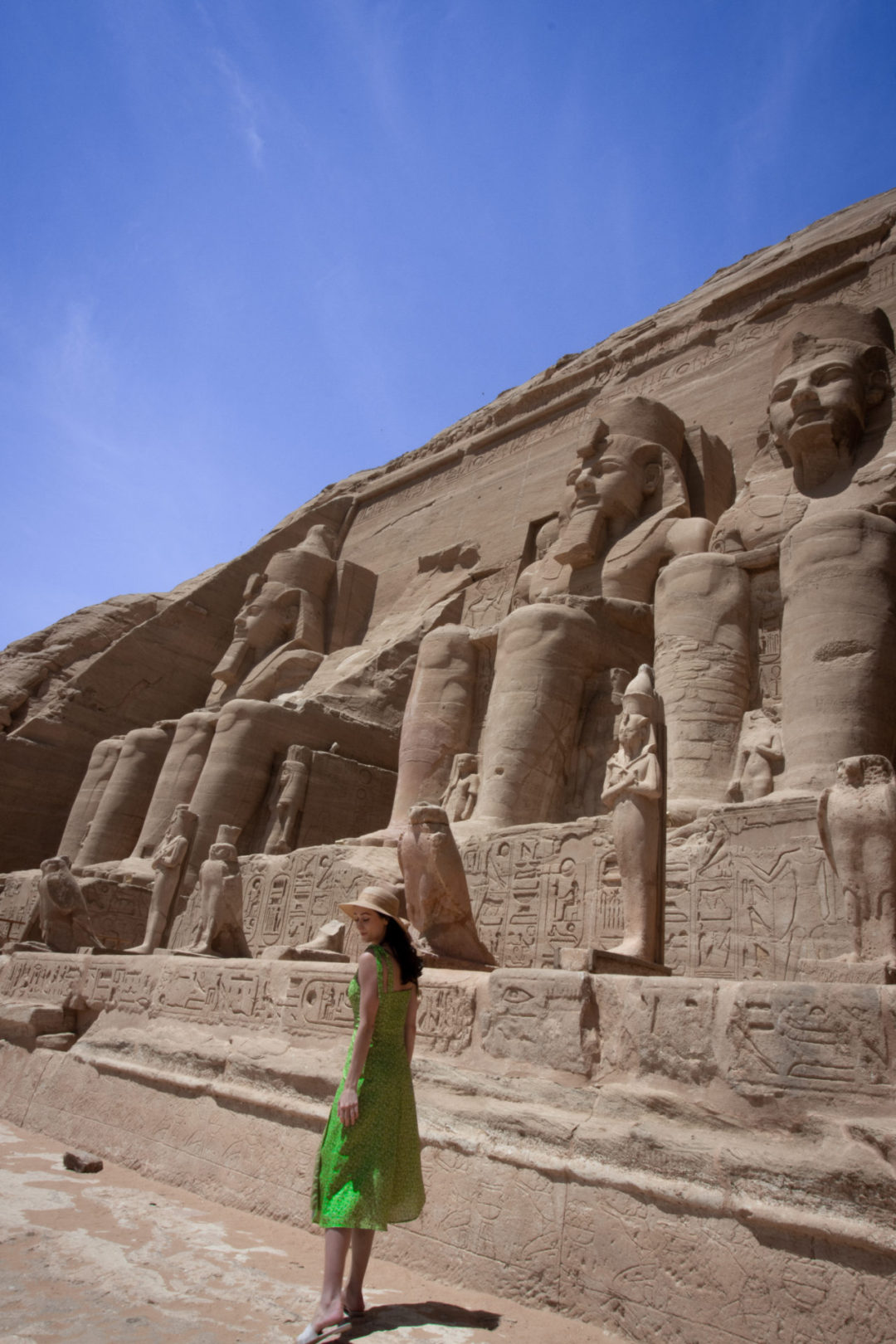Travel Blogger Jordan Gassner standing and smiling near two right statues of Ramses II at the Great Temple of Abu Simbel in Egypt