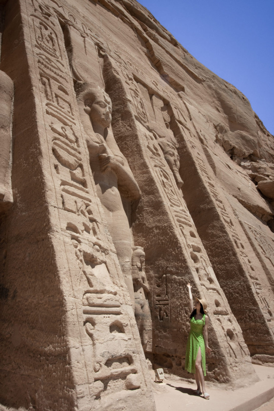 Travel Blogger Jordan Gassner holding up her arms in front of a giant statue of Nefertari at Abu Simbel in Egypt