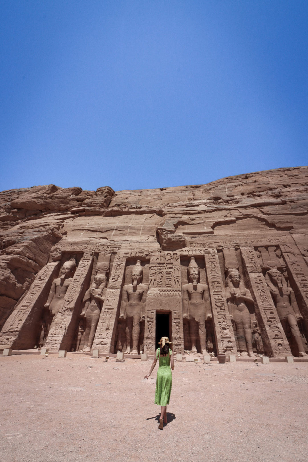 Travel Blogger Jordan Gassner wearing a green dress and straw sunhat walking toward the secondary temple in Egypt's Abu Simbel