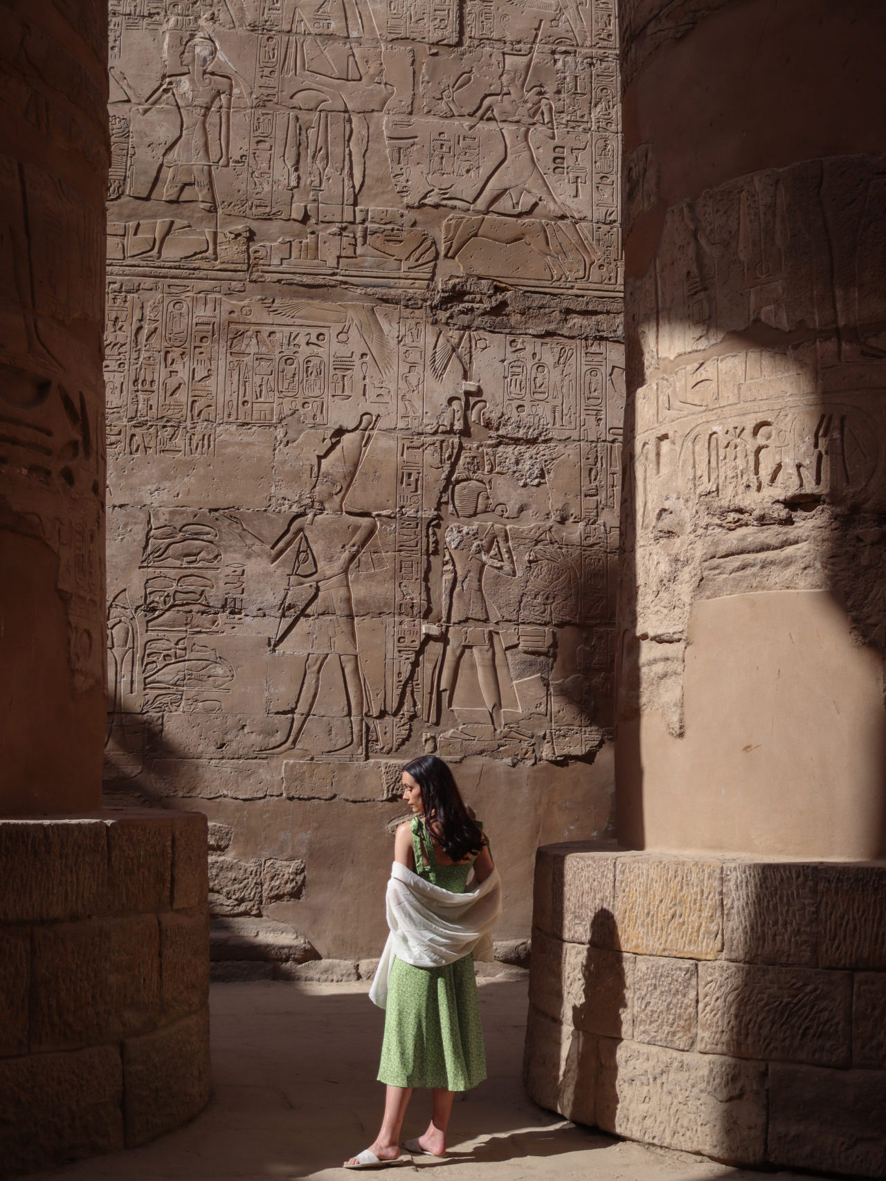 Travel Blogger Jordan Gassner wearing a green dress and standing just outside the shadows from the columns in Karnak Temple's Hypostyle Hall in Luxor, Egypt