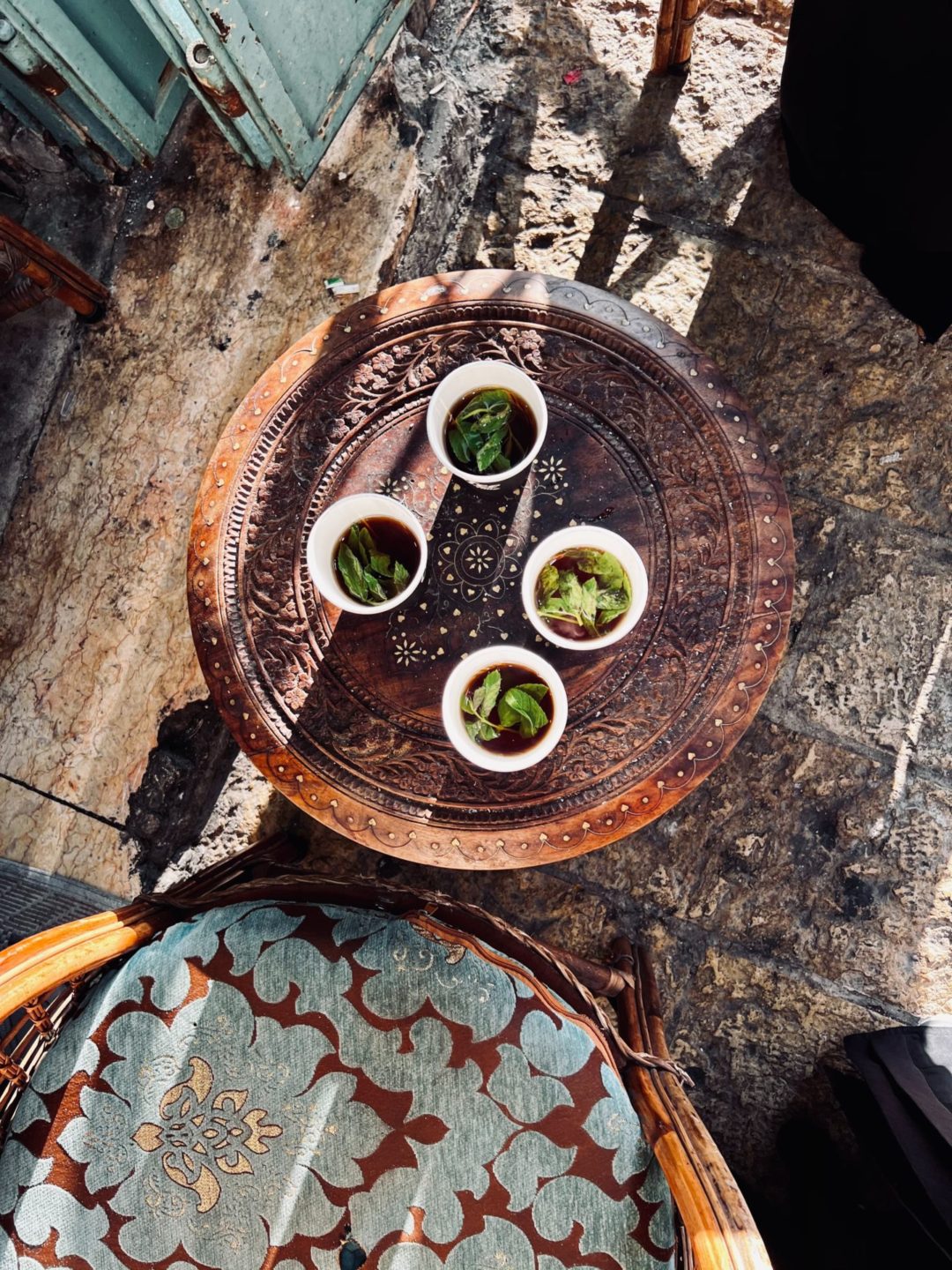 A brass table and straw chair with four cups of mint tea