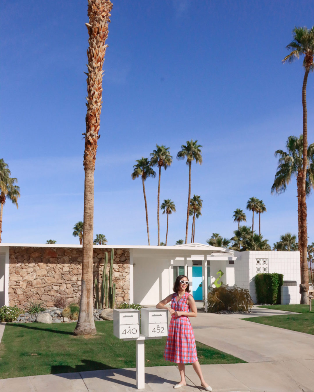 Travel Blogger Jordan Gassner smiling while wearing a vintage dress in front of Alice and Jack's Home from Don't Worry Darling