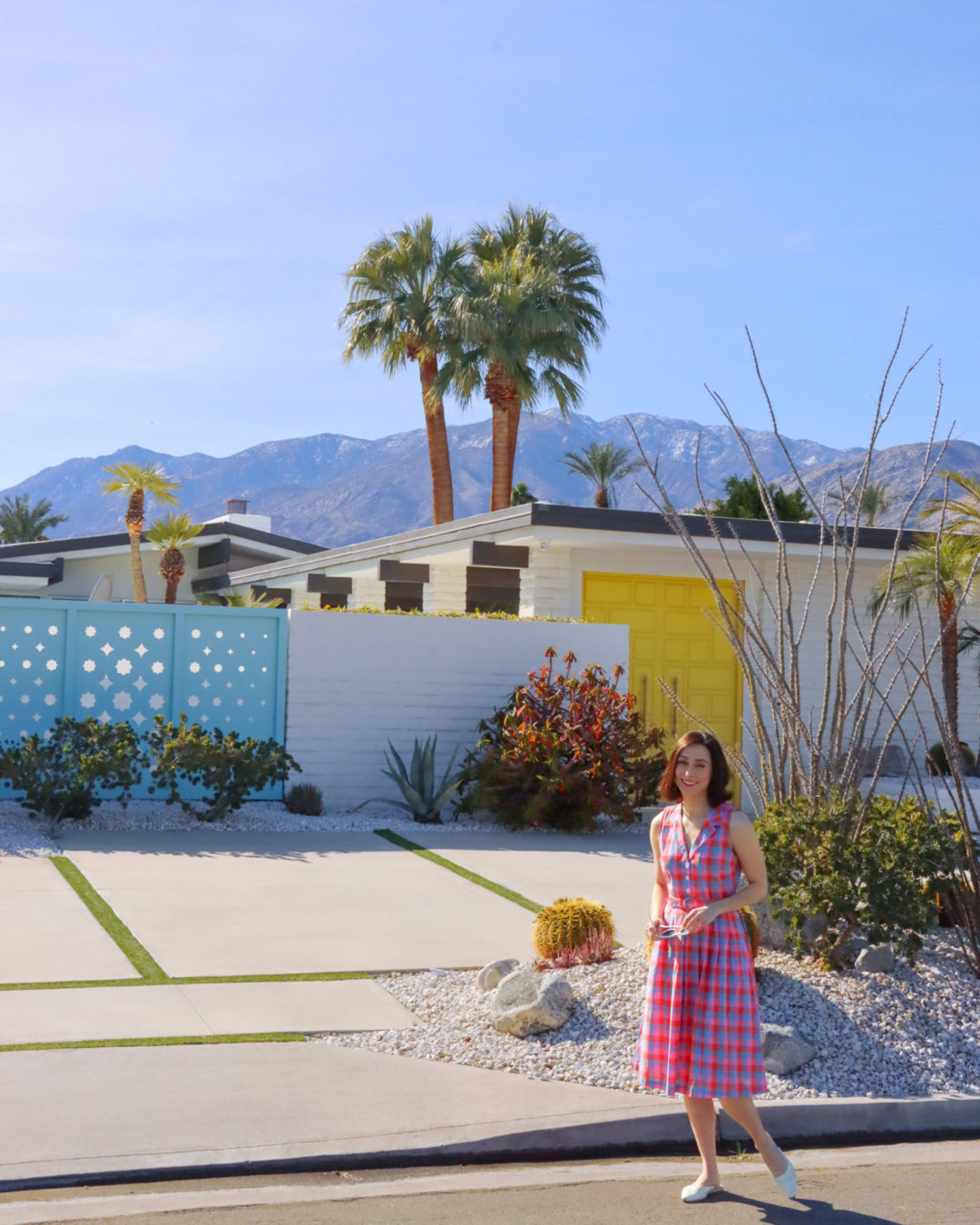 Travel Blogger Jordan Gassner walking away from a mid-century home with a pastel yellow door and light blue gate in Palm Springs