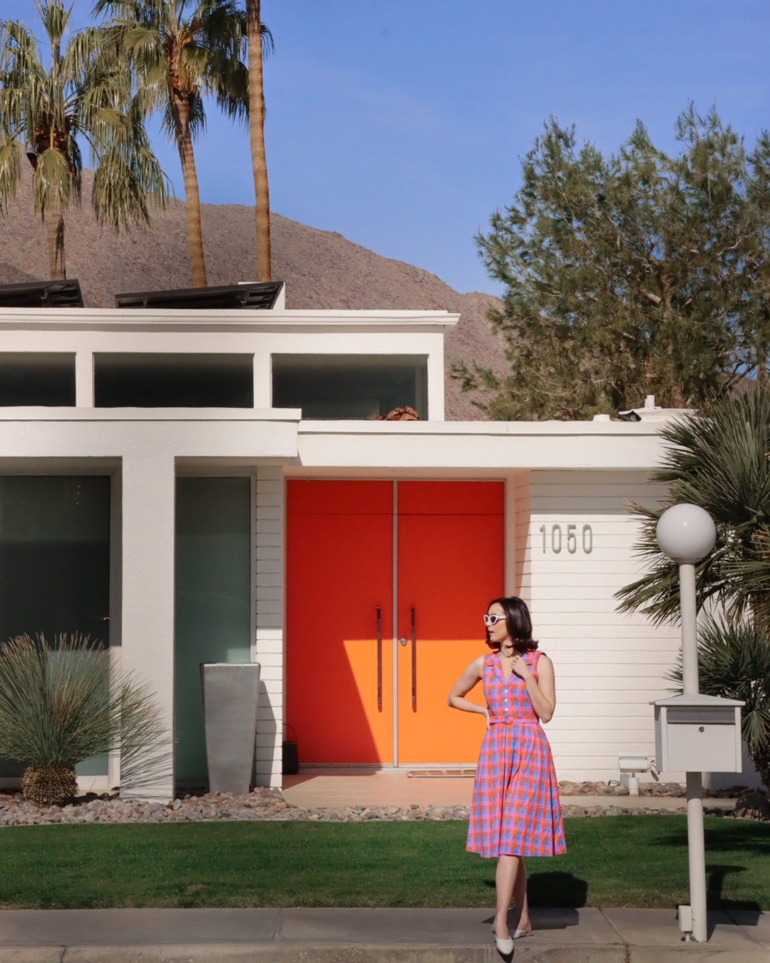 Travel Blogger Jordan Gassner posing in a vintage dress front of a mid-century modern home with orange doors in Palm Springs
