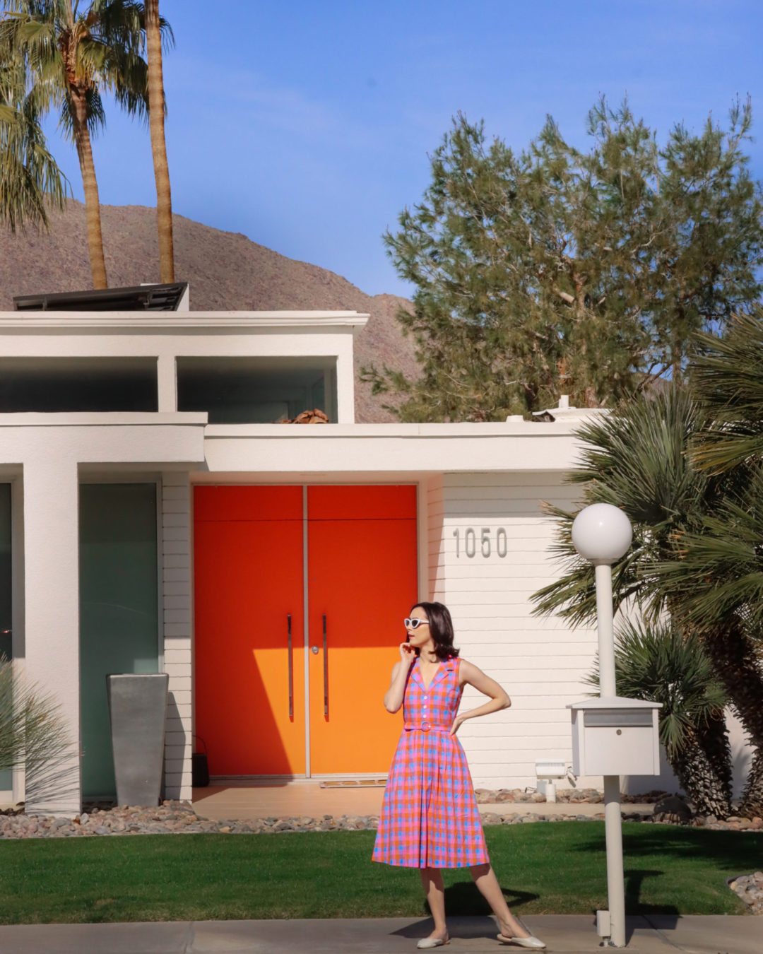 Travel Blogger Jordan Gassner looking sideways while standing in front of a mid-century modern home with orange doors in Palm Springs