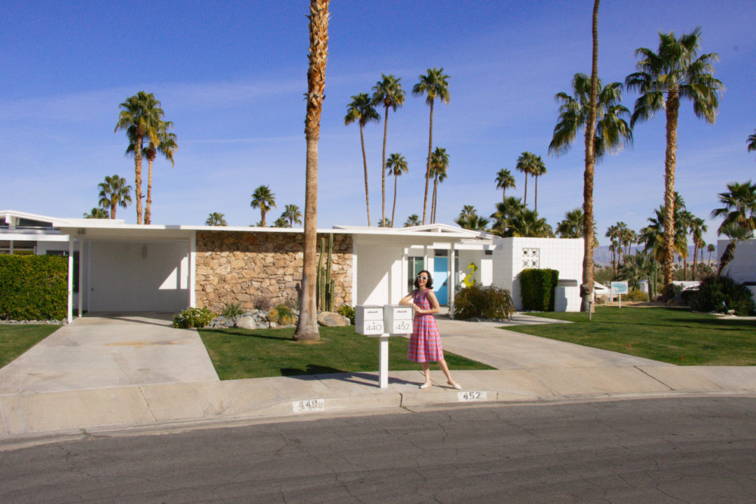 Travel Blogger Jordan Gassner wearing a vintage dress and leaning on a mailbox in front of Alice and Jack's Home from Don't Worry Darling