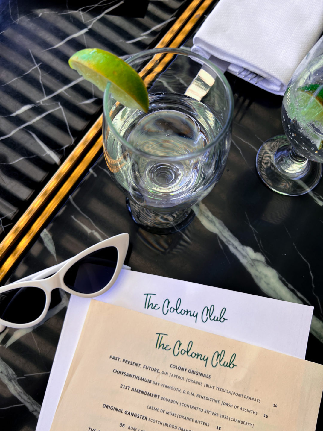Don't Worry Darling Travel Aesthetic: White cat eye sunglasses next to two menus at the Colony Club Restaurant in Palm Springs, California