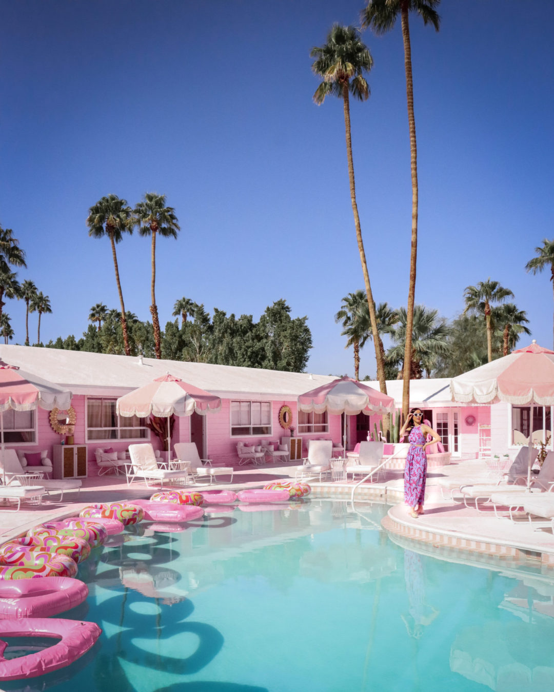 Travel Blogger Jordan Gassner hanging out near a pool filled with pink floaties at the pink Trixie Motel in Palm Springs, California