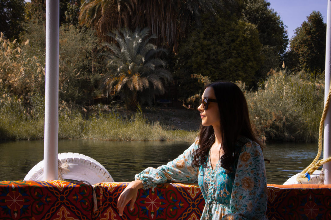 Death on the Nile Travel Guide: Travel Blogger Jordan Gassner peering out on a covered motor boat while traveling on the Nile River in Egypt