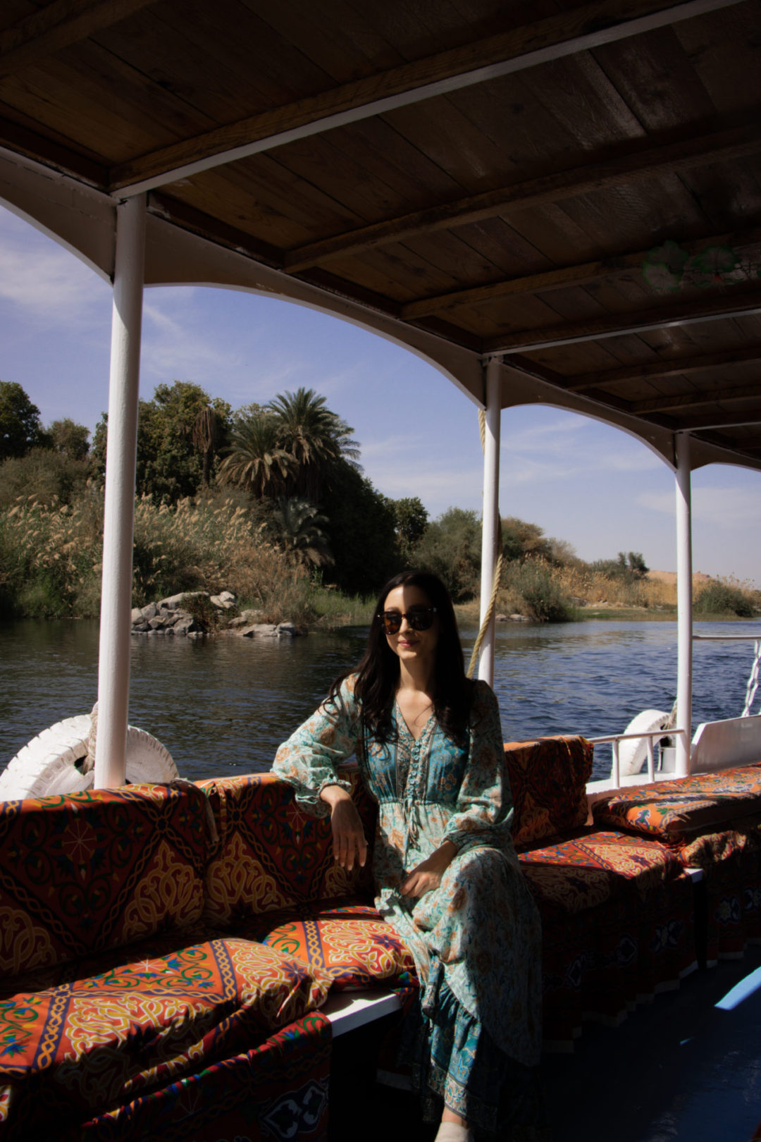 Death on the Nile Travel Guide: Travel Blogger Jordan Gassner smiling from a seat on a covered, open-air boat on the Nile River in Aswan, Egypt
