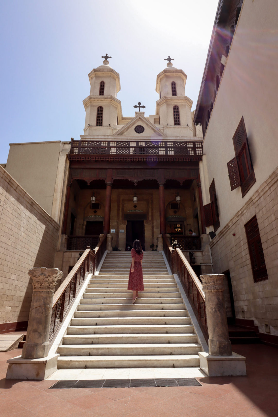 Travel Blogger Jordan Gassner walking up the steps of Egypt's Hanging Church while wearing a burnt red midi dress