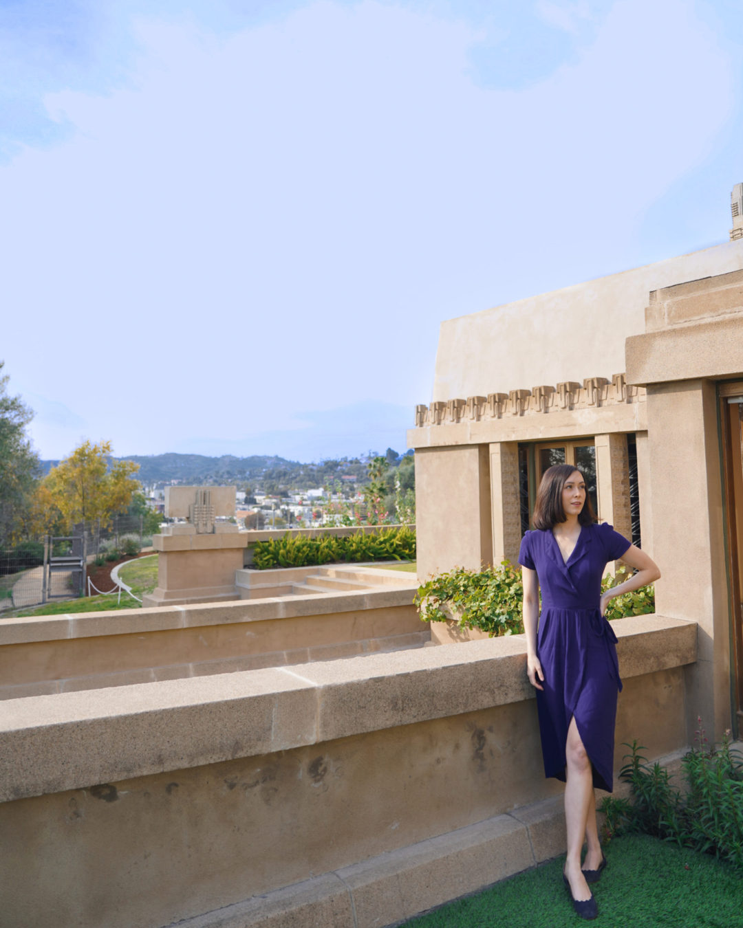 Travel Blogger Jordan Gassner standing with hand on hip outside a doorway in the backyard of Hollyhock House in Los Angeles