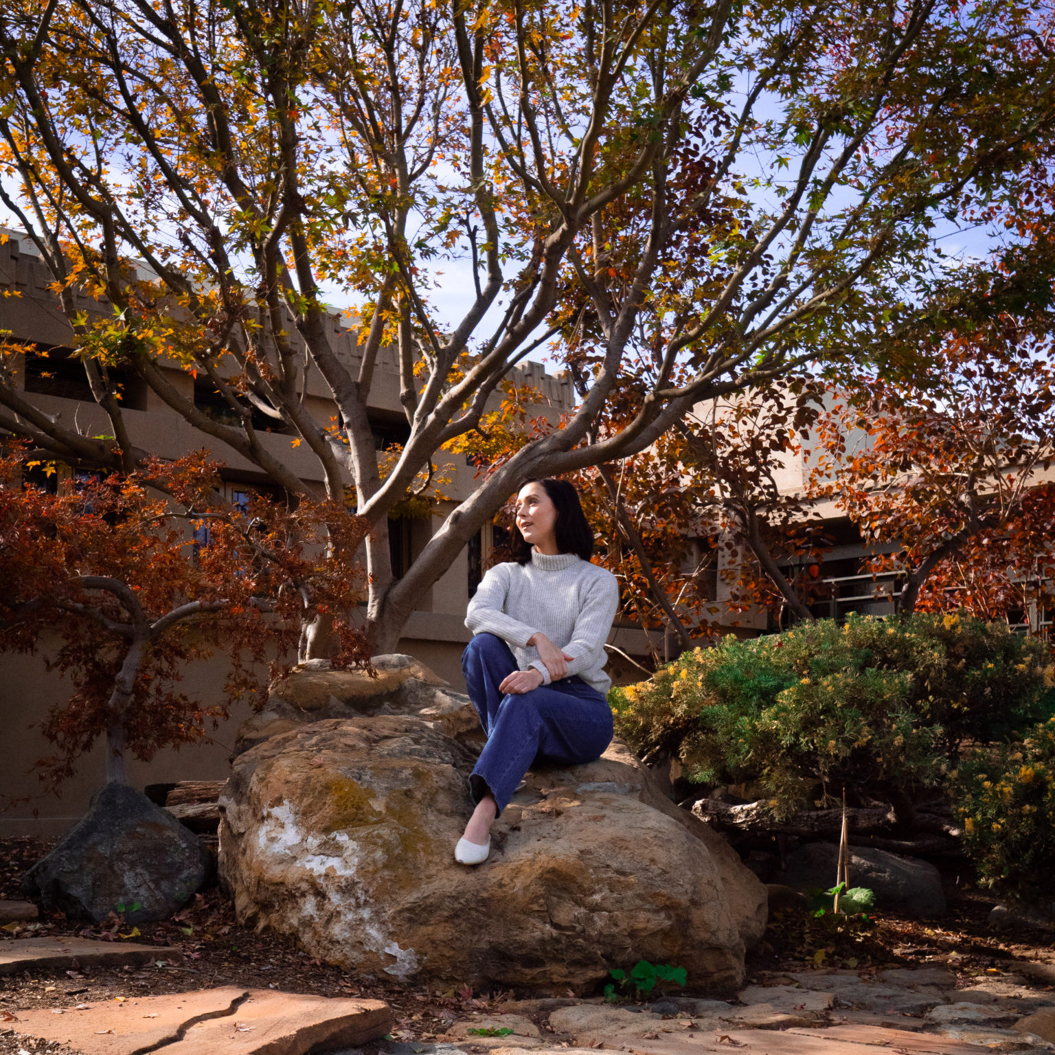 Travel Blogger Jordan Gassner smiling while sitting on a rock in LA's Barnsdall Park just in front of Hollyhock House