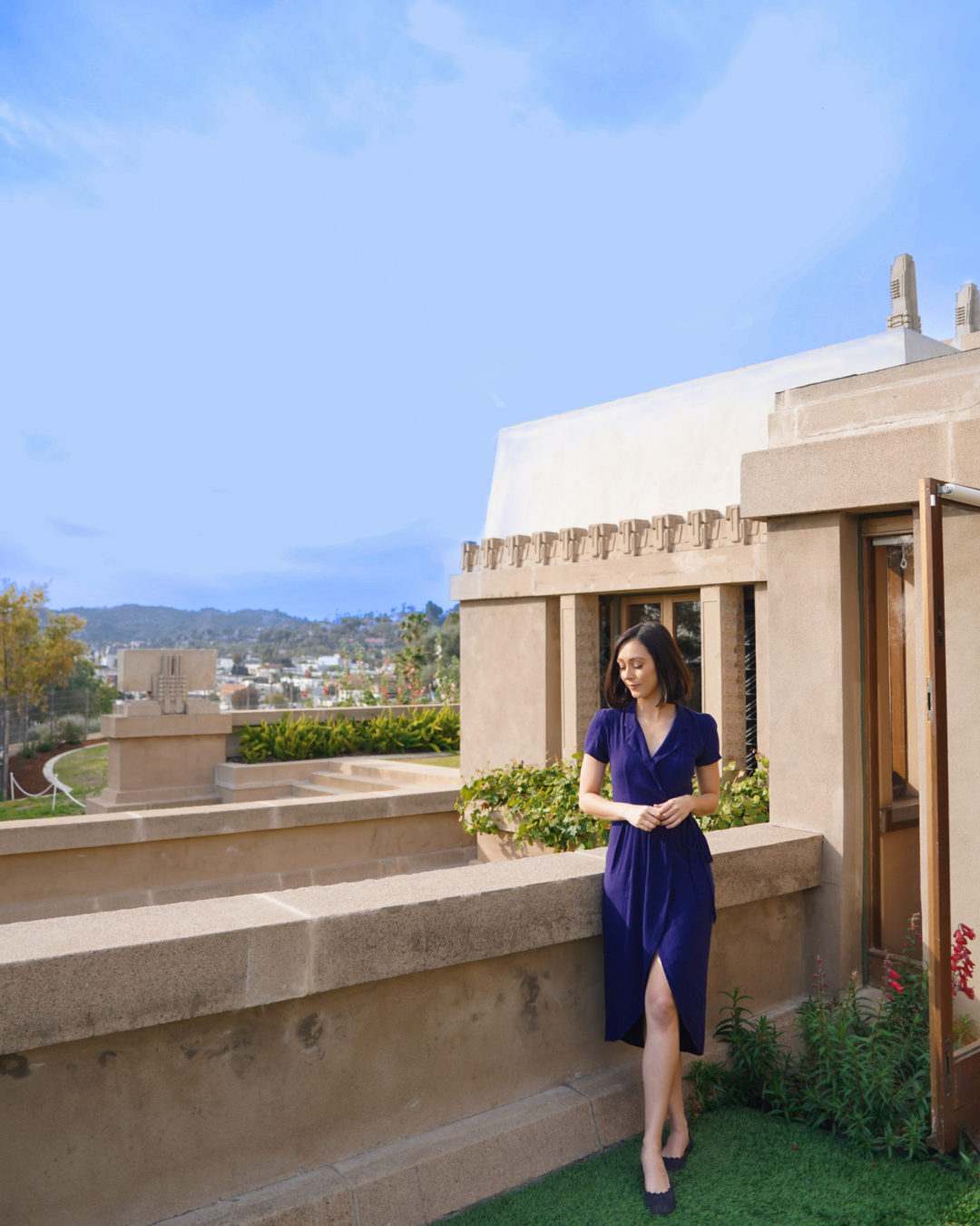 Travel Blogger Jordan Gassner clasping her hands while standing outside a doorway in the backyard of Hollyhock House in Los Angeles