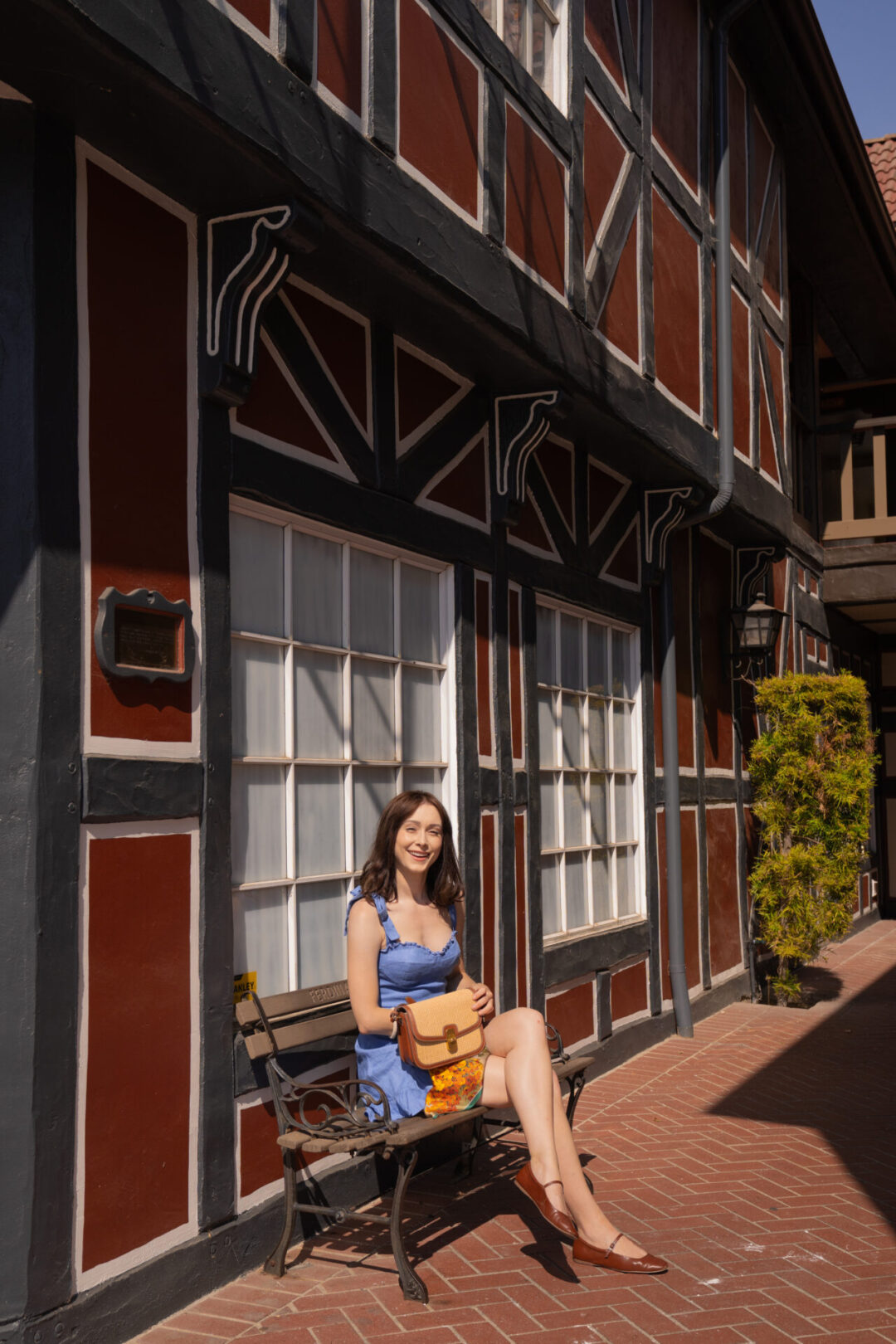 Travel Blogger Jordan Gassner smiling while sitting on a bench in front of a Danish-style building in Solvang, California