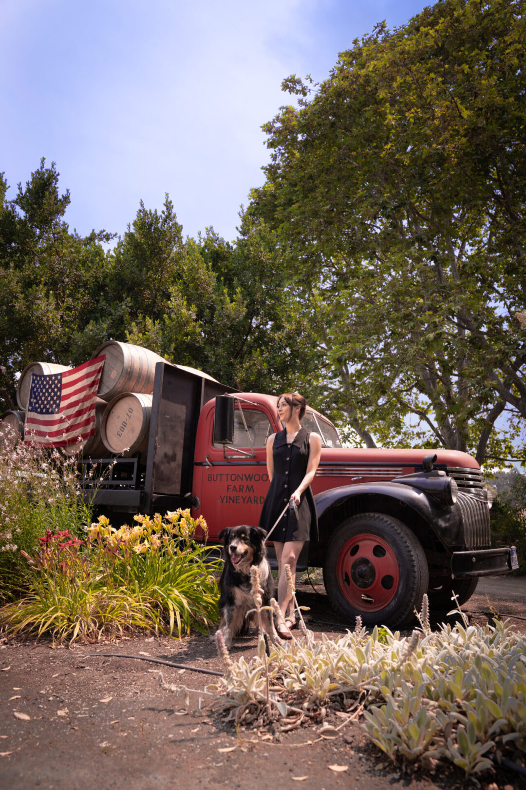 Travel Blogger Jordan Gassner and dog standing in front of a vintage red truck at the Buttonwood Farm Tasting Room in Solvang, California