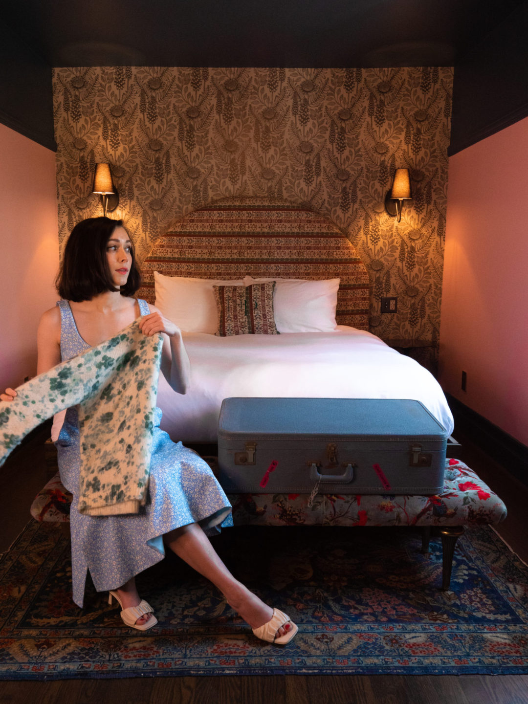 Travel Blogger Jordan Gassner looking out the window and folding a shirt while seated in front of a bed at Noble + Proper in Big Bear, California