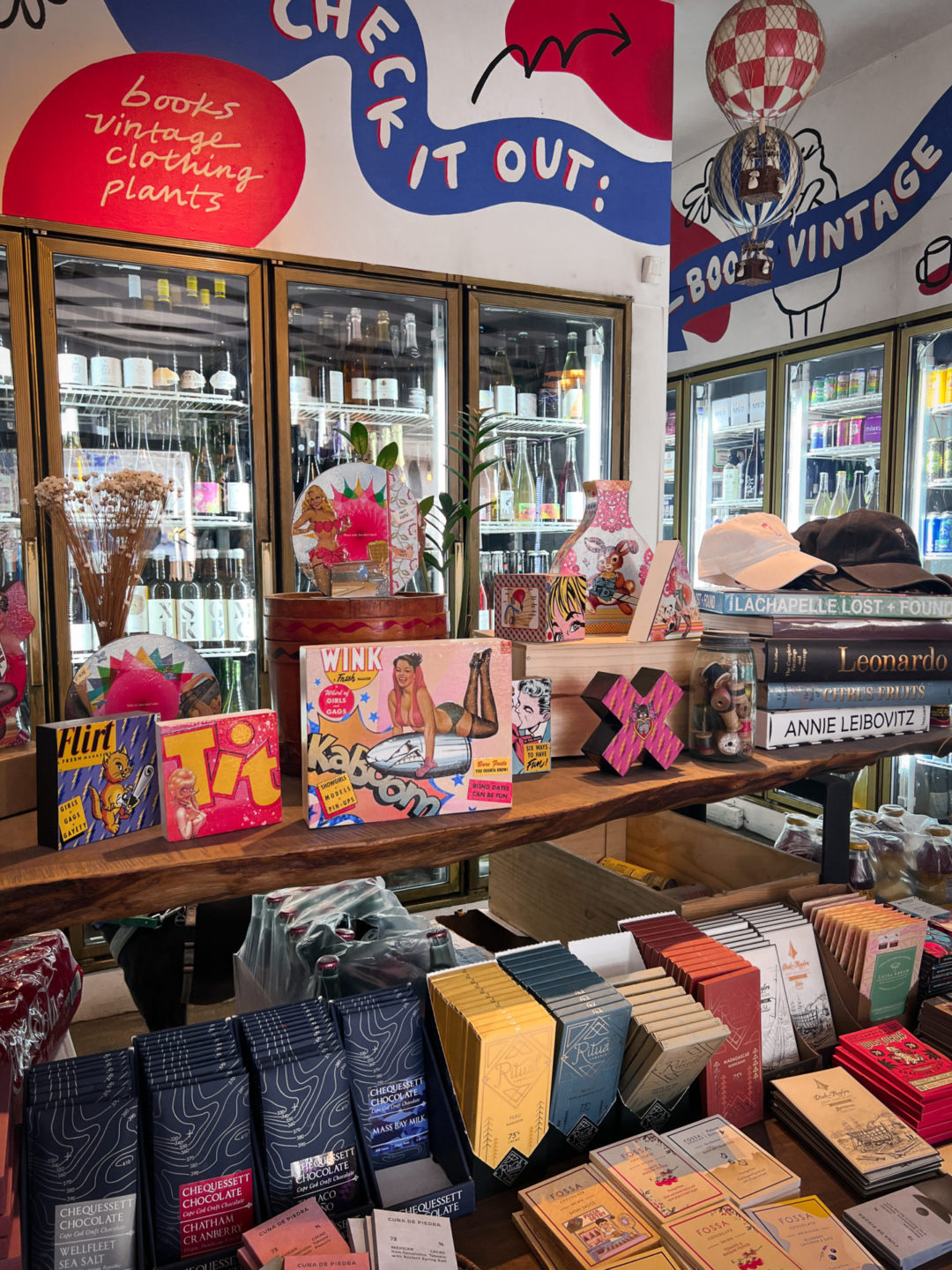 A display table with cookbooks, and chocolates in front of a refrigerator full of chilled wines inside Vin On Rose in Venice, California
