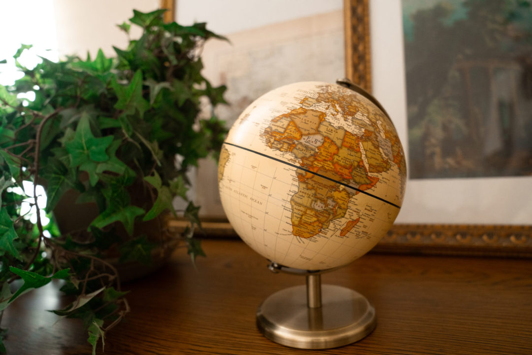 A small vintage globe sitting in front of a plant and two paintings