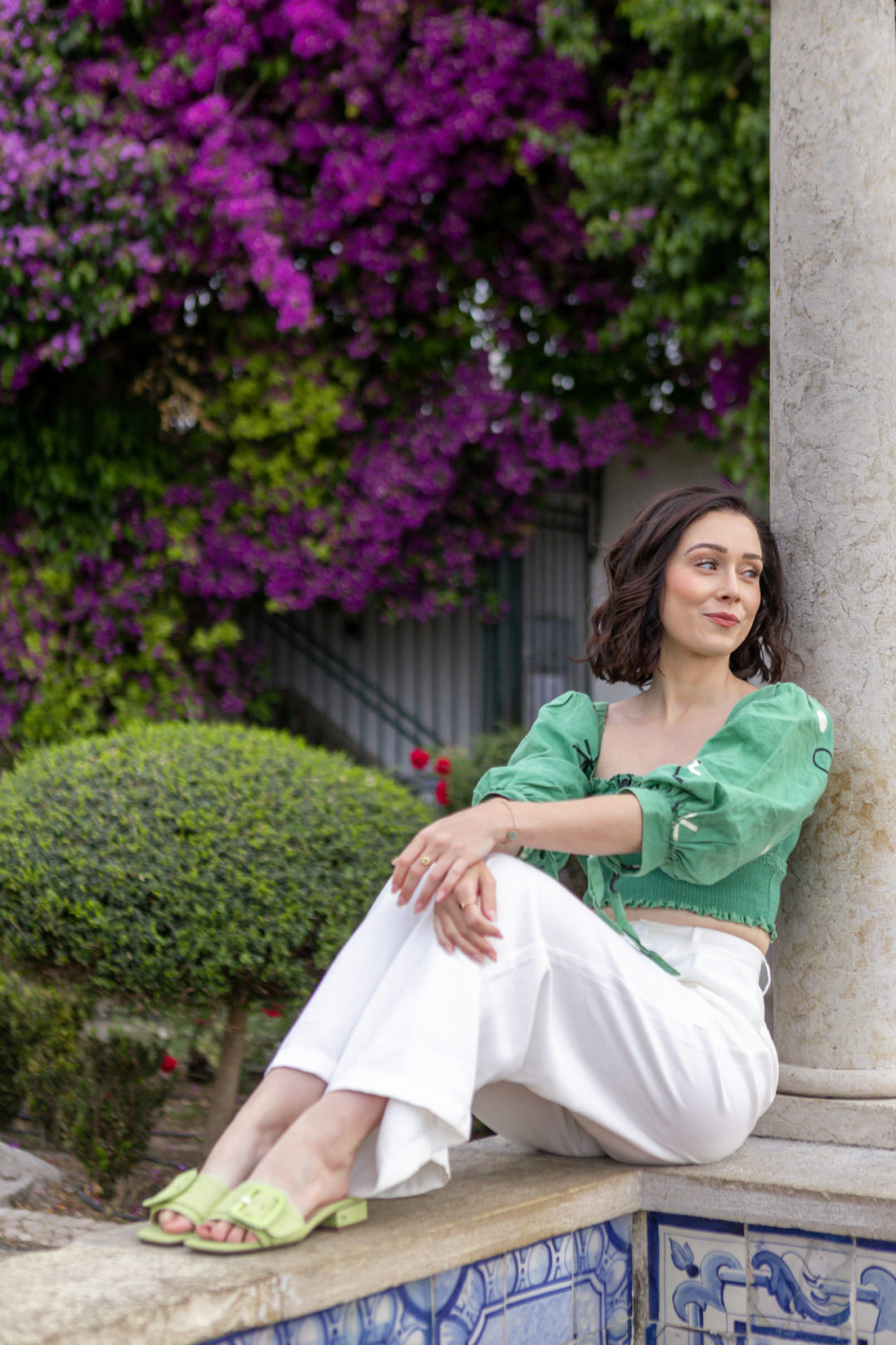 Jordan Gassner sitting and smiling on a ledge of Lisbon's Miradouro de Santa Luzia, with bougainvillea and roses in the background