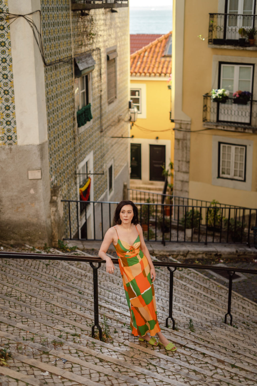 A high angle photo of Travel Blogger Jordan Gassner leaning against a stair railing in a Faithfull the Brand dress in Lisbon, Portugal