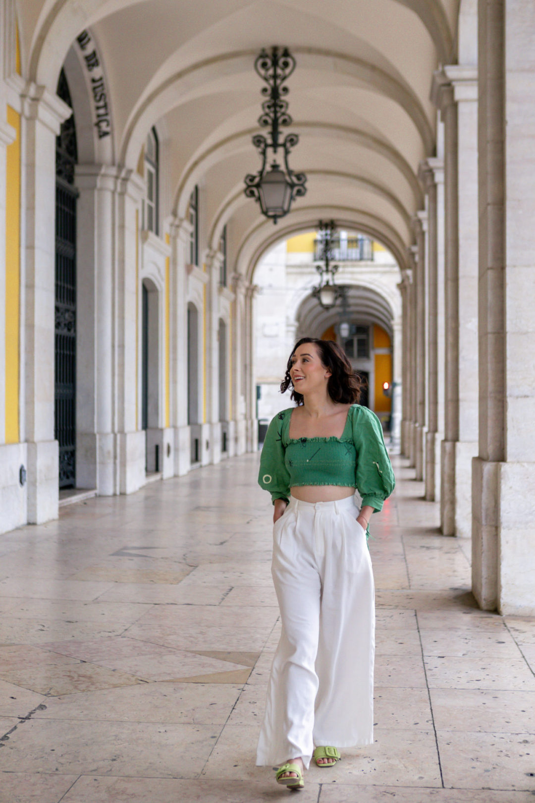 Travel Blogger Jordan Gassner smiling while walking with her hands in her pockets underneath the Arco da Rua Augusta in Lisbon