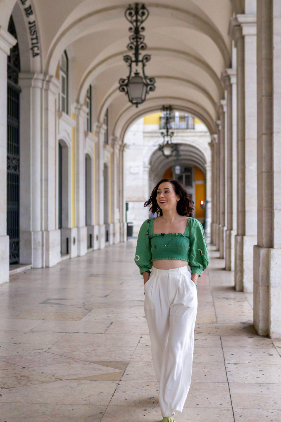 Travel Blogger Jordan Gassner laughing with her hands in her pockets while walking underneath the Arco da Rua Augusta in Lisbon