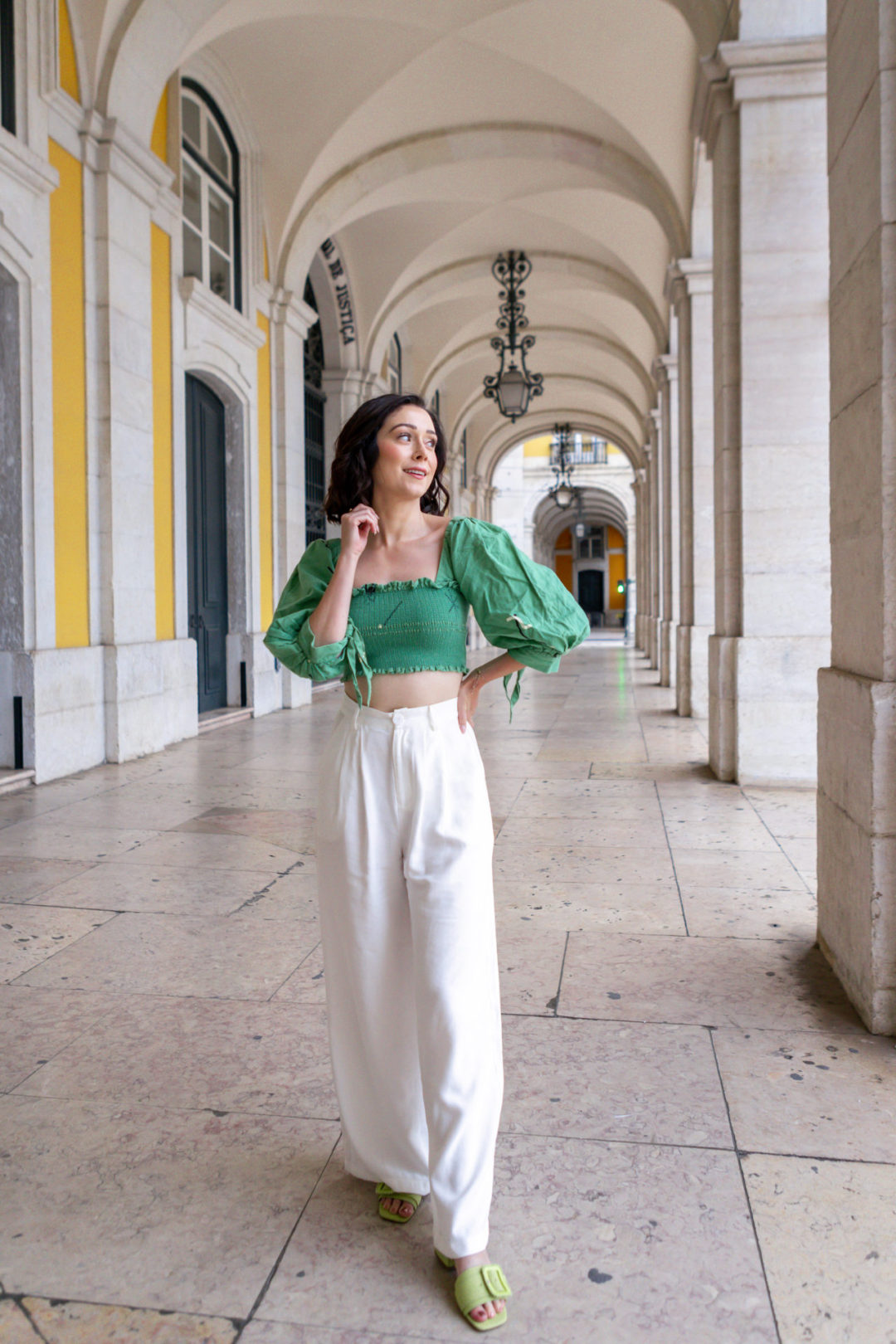 Jordan Gassner looking toward Praça do Comércio and smiling from underneath the Arco da Rua Augusta, one of her favorite spots to take photos in Lisbon