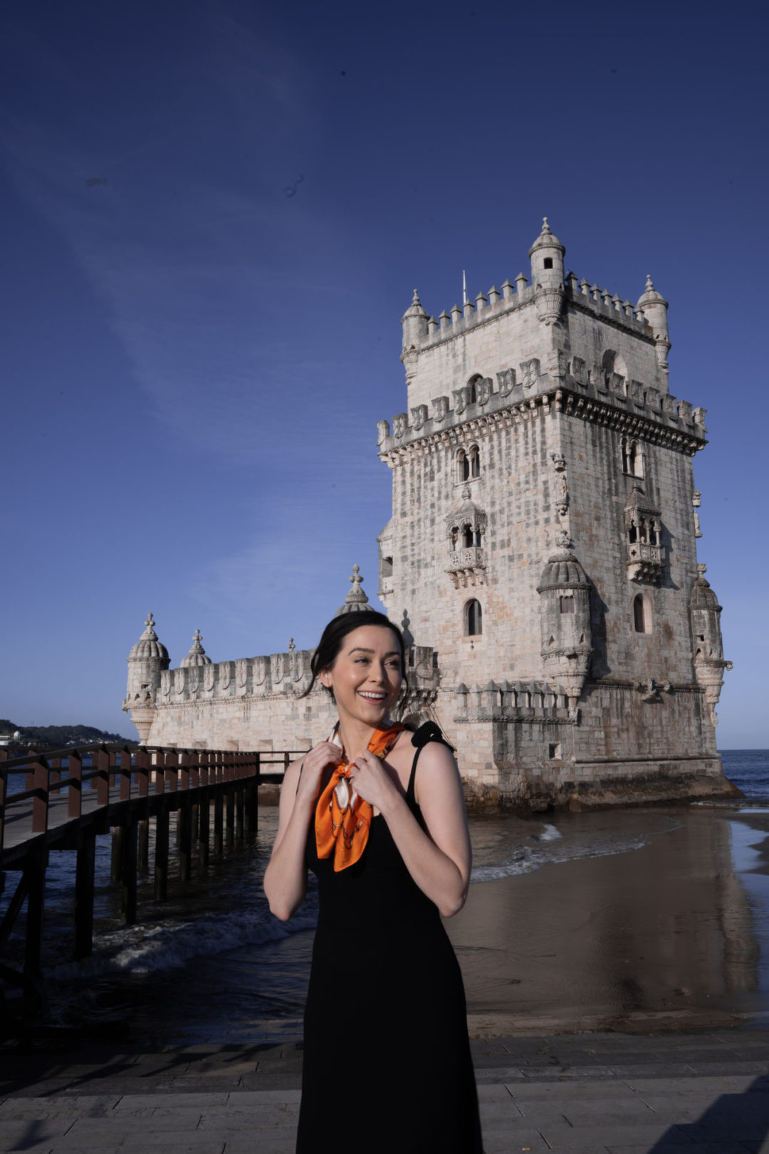 Lisbon Travel Guide: Travel Blogger Jordan Gassner smiling in front of Lisbon's Belem Tower while holding an orange bandana
