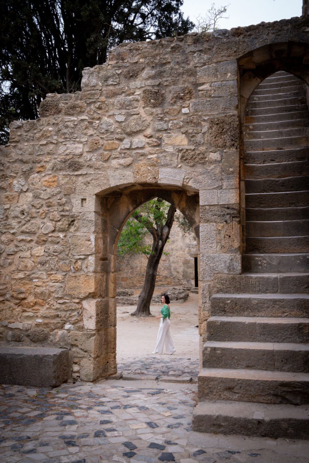 Travel Blogger Jordan Gassner walking through an open area inside Sao Jorge Castle as seen from the other side of a stone archway
