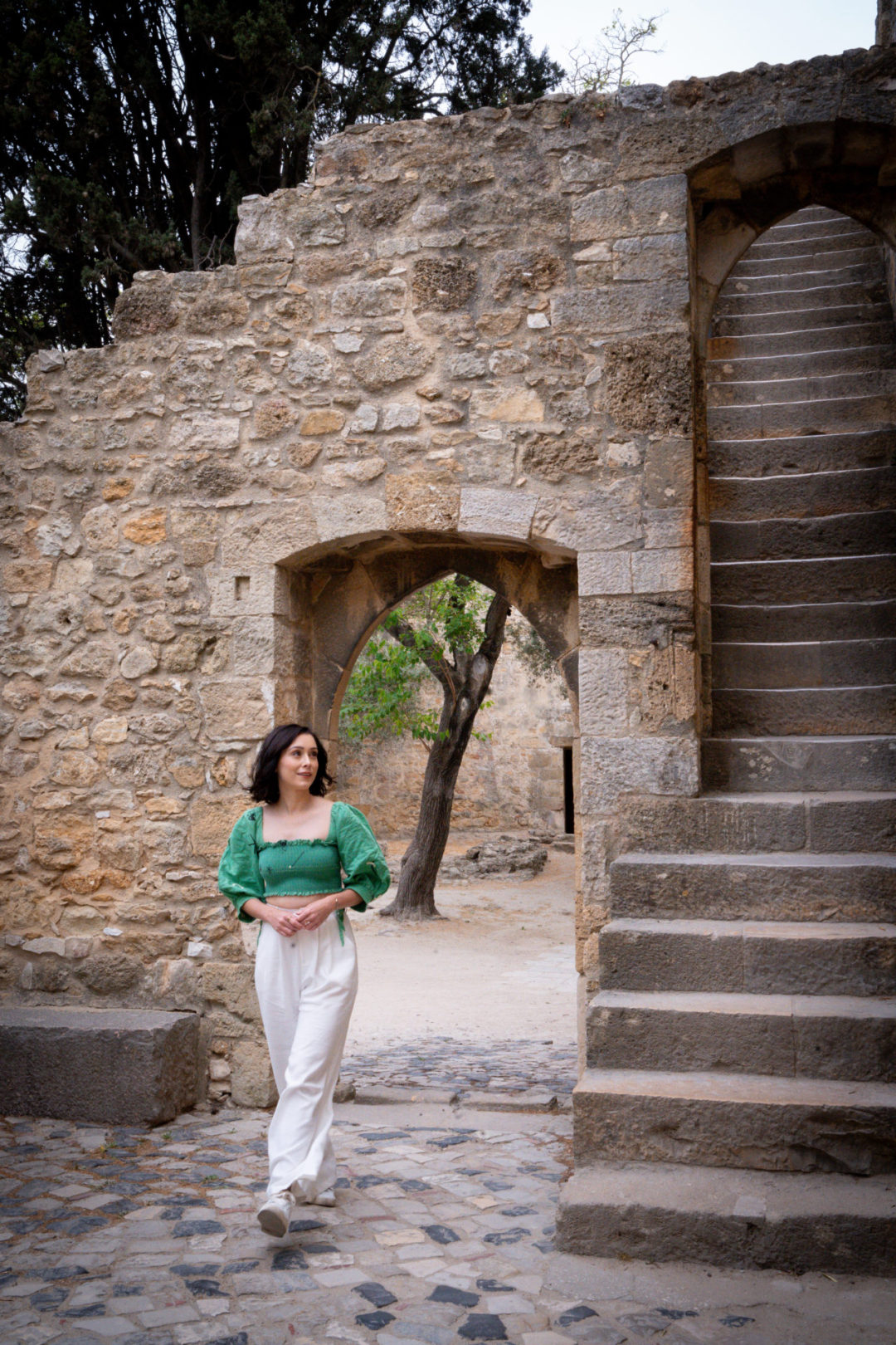 Travel Blogger Jordan Gassner walking under an arch near a staircase inside Sao Jorge Castle in Lisbon, Portugal