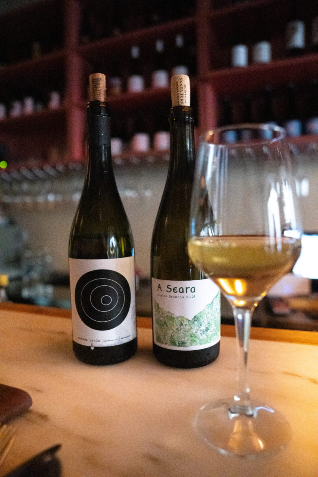 Two bottles of natural wine and a glass of white wine on the bar at Dahlia, a natural wine and tapas bar in Lisbon, Portugal