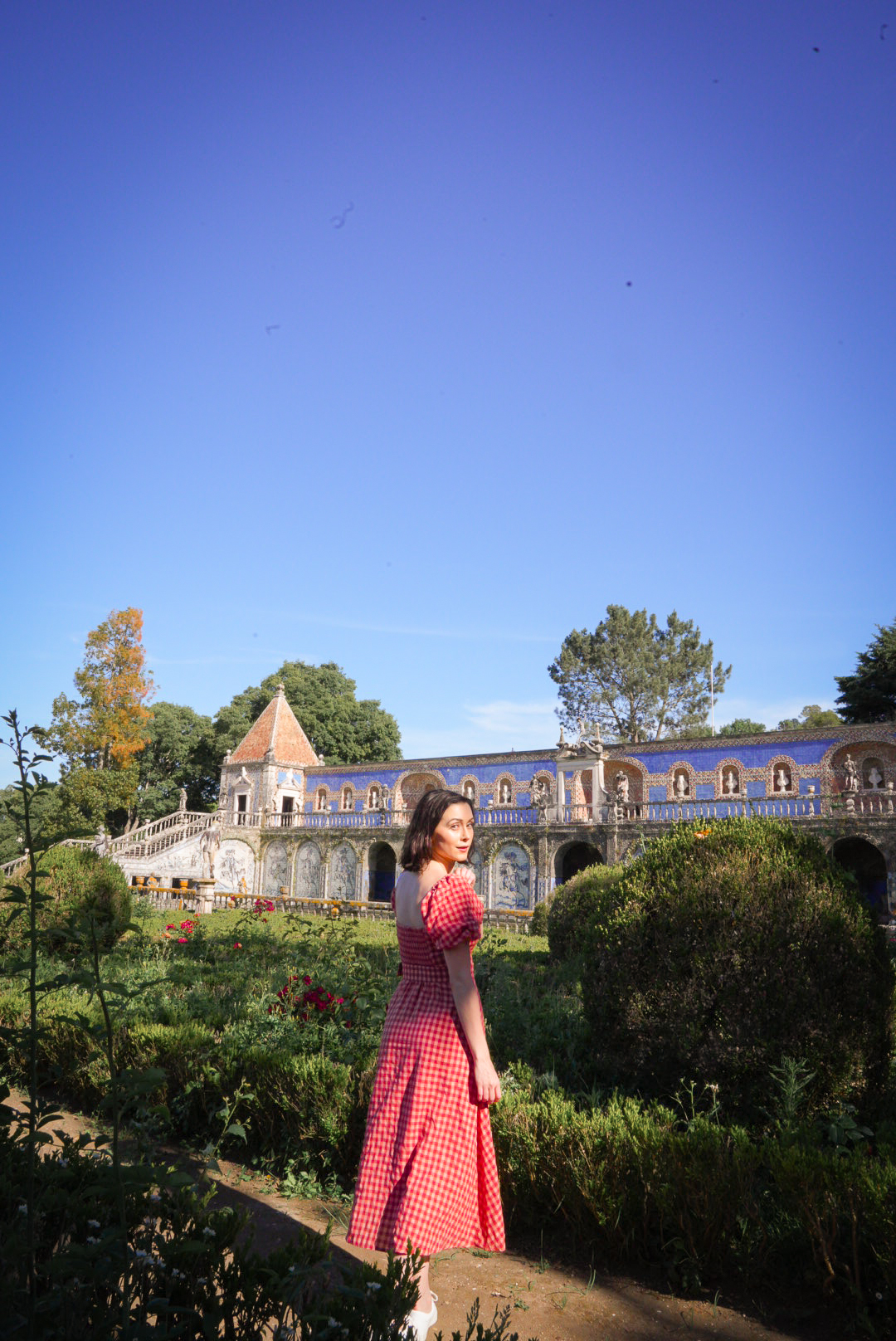 Travel Blogger Jordan Gassner looking over her shoulder and from a shaded pathway in the Palace Fronteira Gardens in Lisbon, Portugal