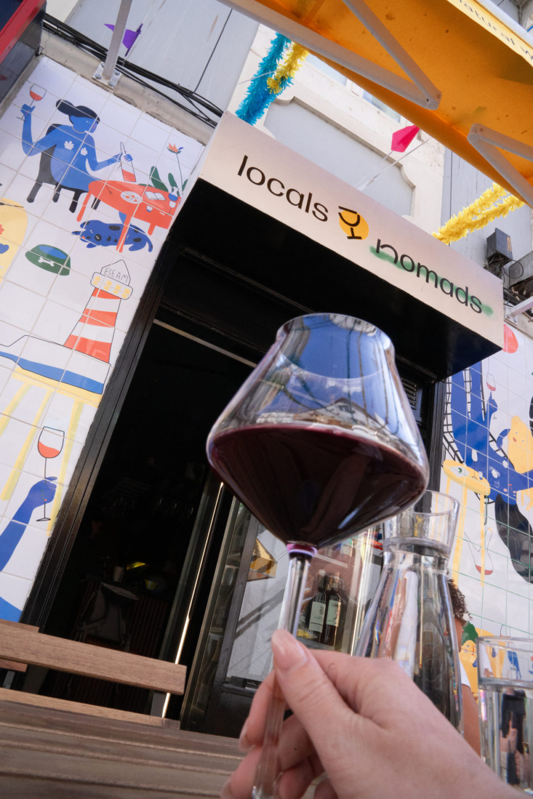 Travel Blogger Jordan Gassner holding a glass of red wine at a table outside Locals & Nomads natural wine bar in Lisbon, Portugal