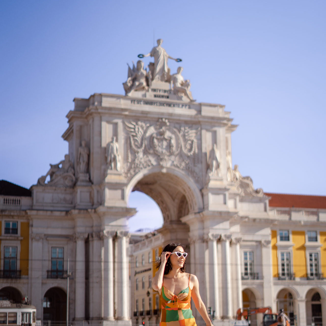 Travel Blogger Jordan Gassner wearing white sunglasses and smiling while walking through Praça do Comércio in Lisbon, Portugal