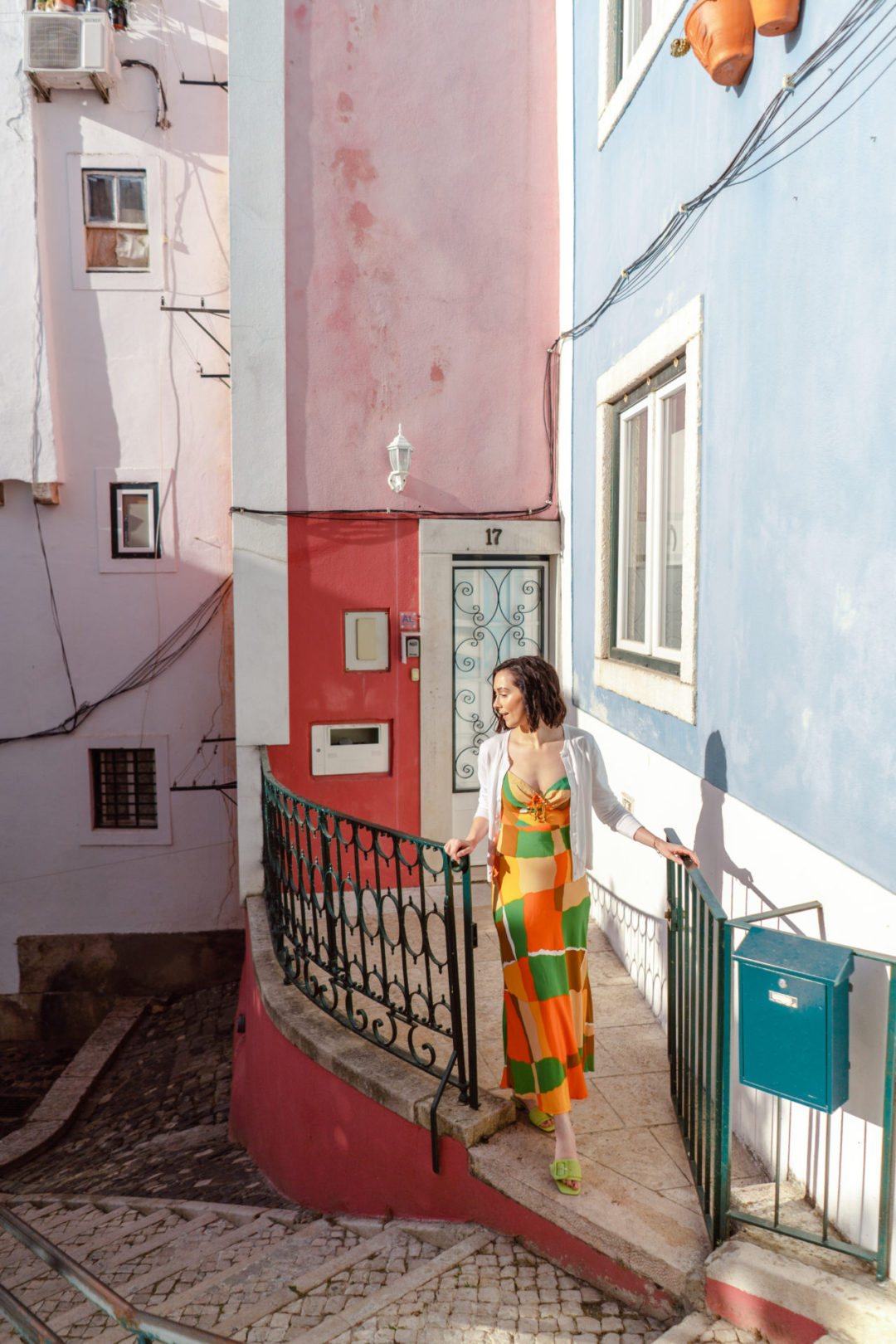 Travel Blogger Jordan Gassner exiting a gated porch in front of a pink, red and baby blue building in Lisbon, Portugal's Alfama neighborhood