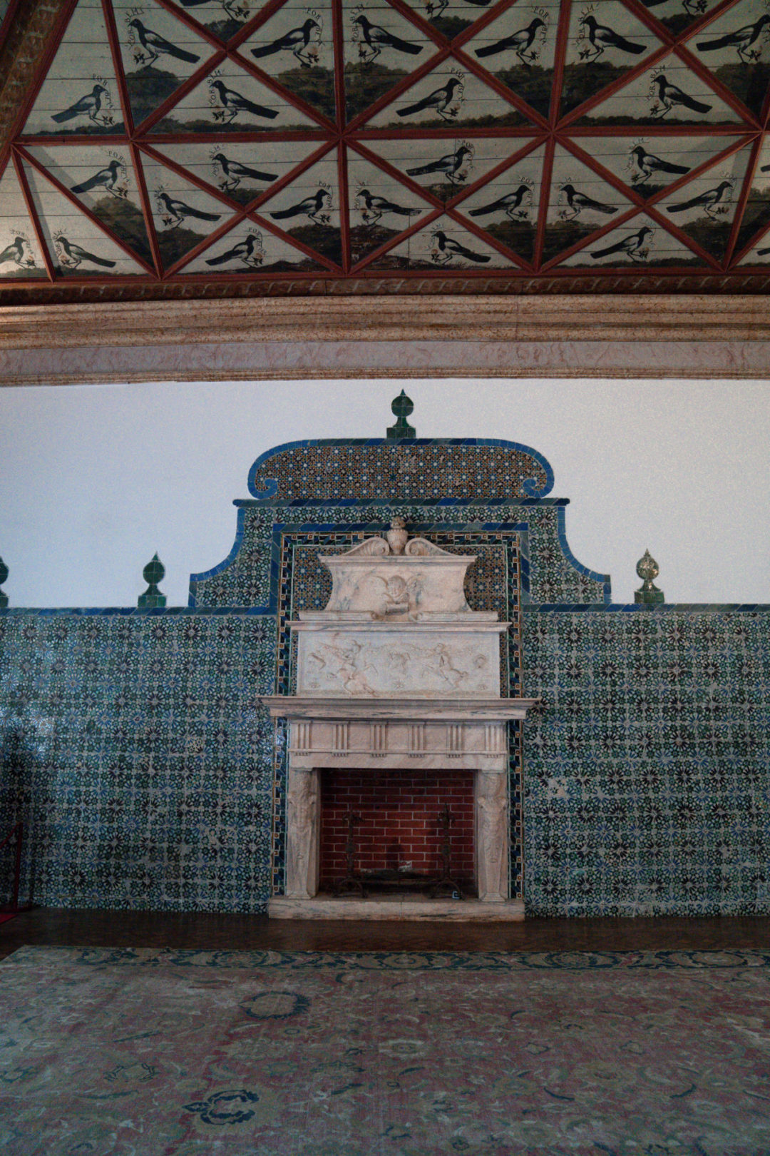 A room inside Sintra's National Palace with a stone fireplace, a wall of azulejo tiles, and a bird-motif patterned ceiling