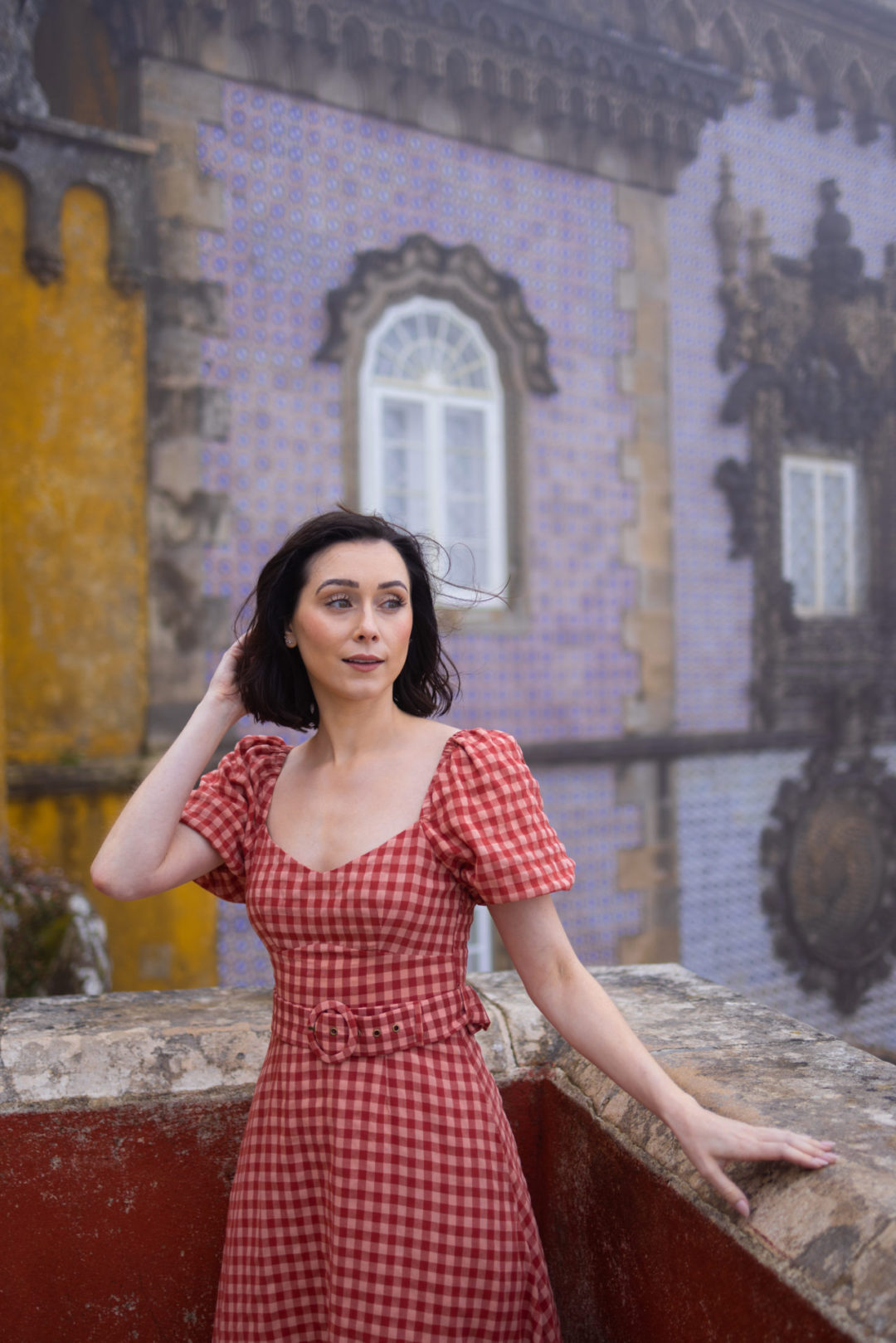 Travel Blogger Jordan Gassner looking out over a balcony at the red, yellow and blue Pena Palace in Sintra