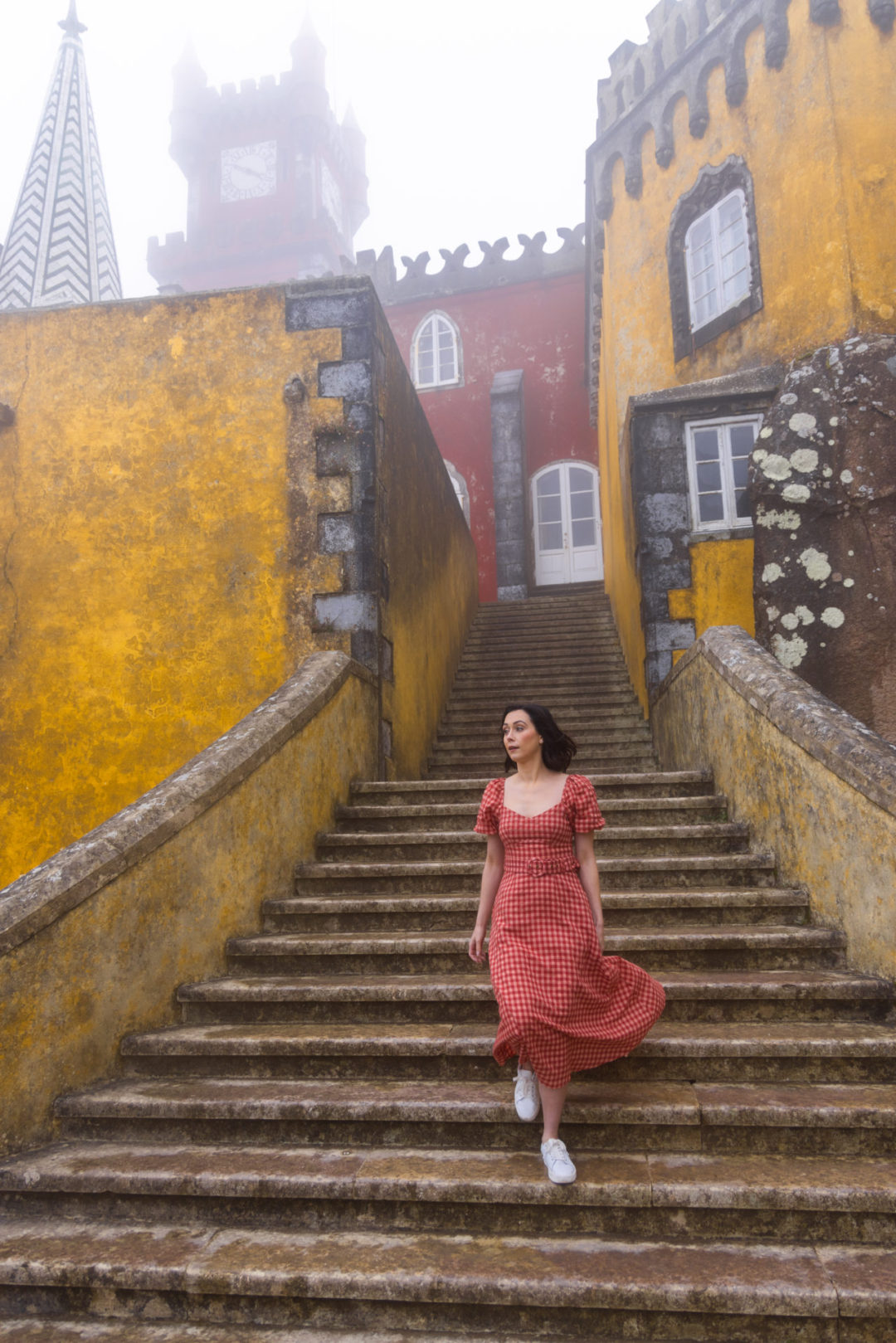Travel Blogger Jordan Gassner walking down the stairs outside the red and yellow Pena Palace in Sintra, Portugal