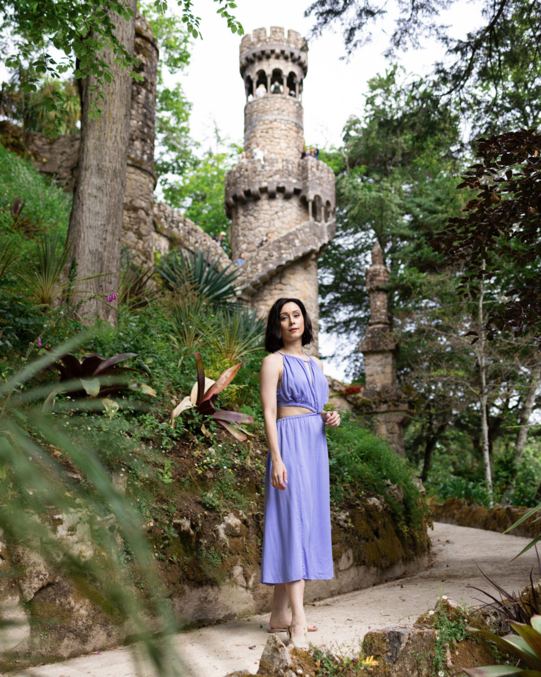 Travel Blogger Jordan Gassner wearing a purple dress in front of a Rapunzel-style tower in Quinta Da Regaleira in Sintra, Portugal