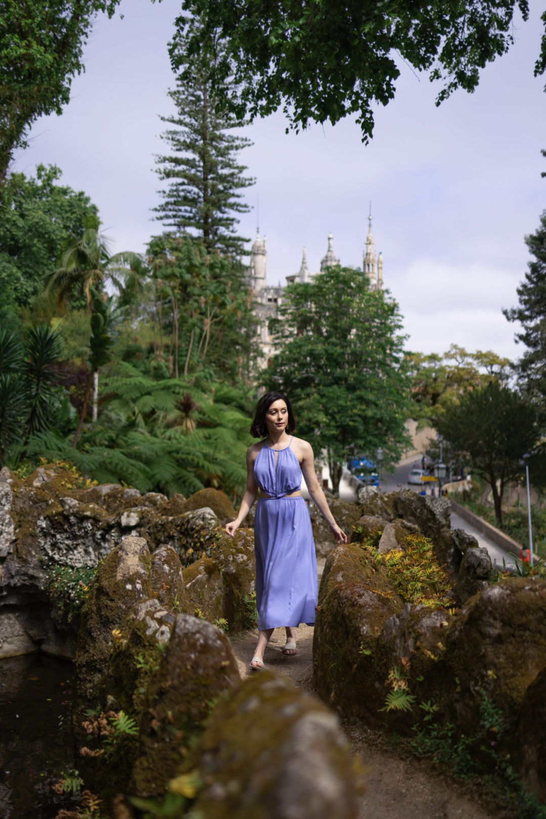Travel Blogger Jordan Gassner walking through the gardens of Quinta Da Regaleira in a purple dress while visiting Sintra, Portugal