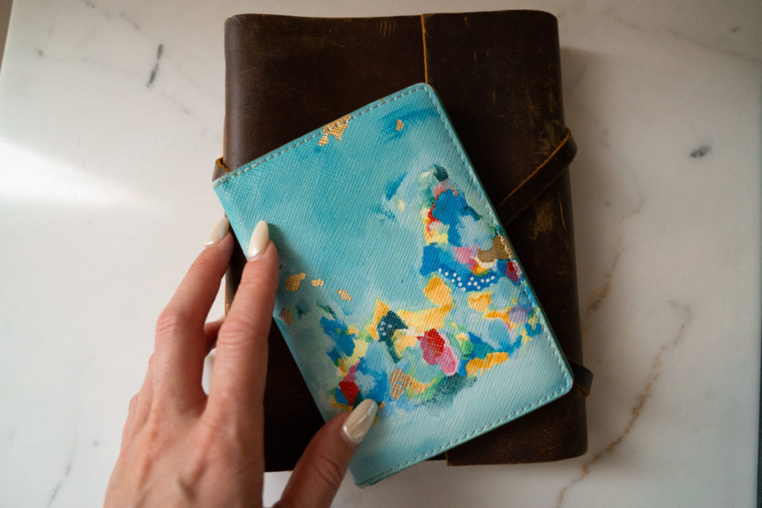 Jordan's hand holding a passport case and travel journal