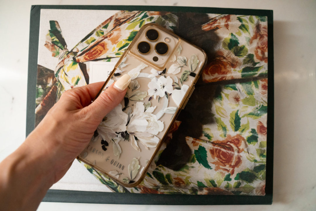 Jordan's hand reaching for an iPhone in a floral print phone case on top of a stack of books
