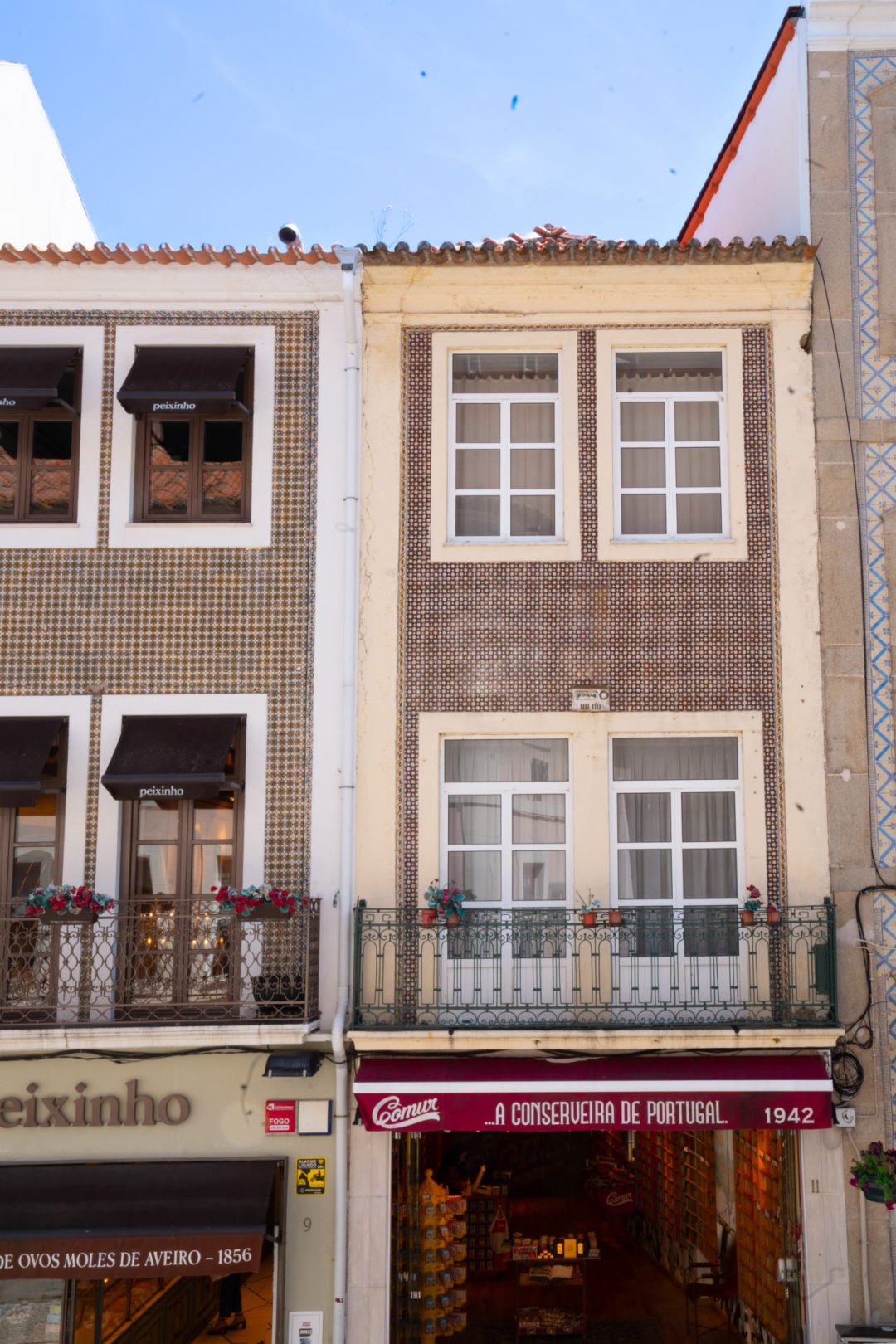 A brown and beige set of buildings with maroon awnings on a clear day in Aveiro, Portugal