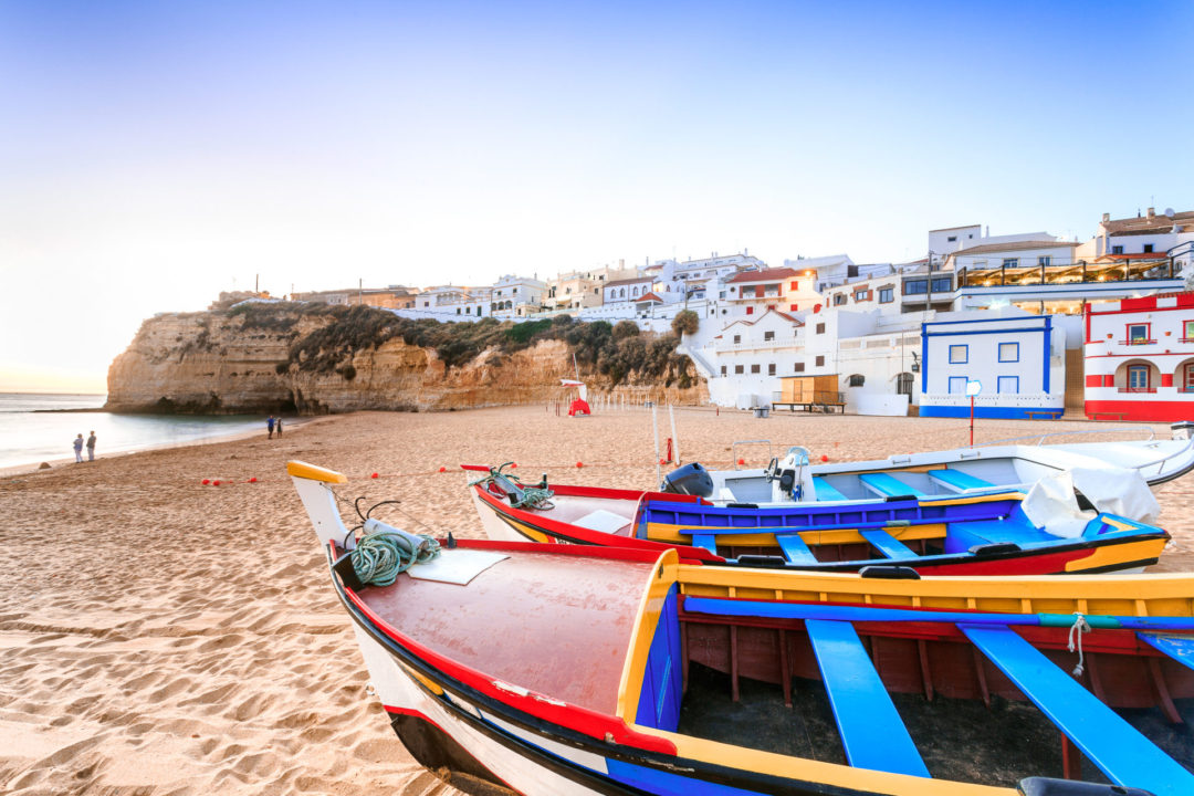 Vividly-painted red, yellow and blue boats sitting on a beach of the Algarve Coast in Carvoeiro, Portugal