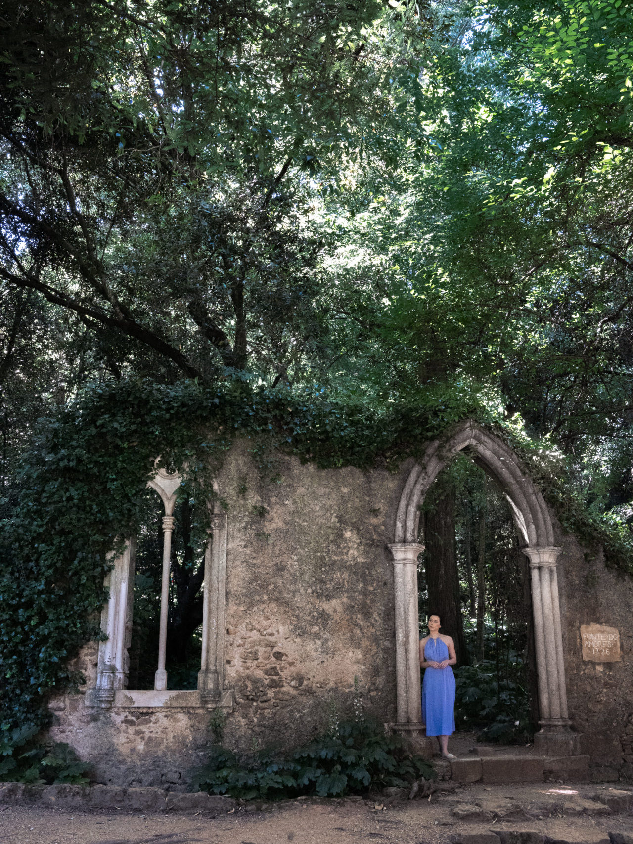 Travel Blogger Jordan Gassner peering out from a medieval archway inside Jardins da Quinta das Lágrimas in Coimbra, Portugal